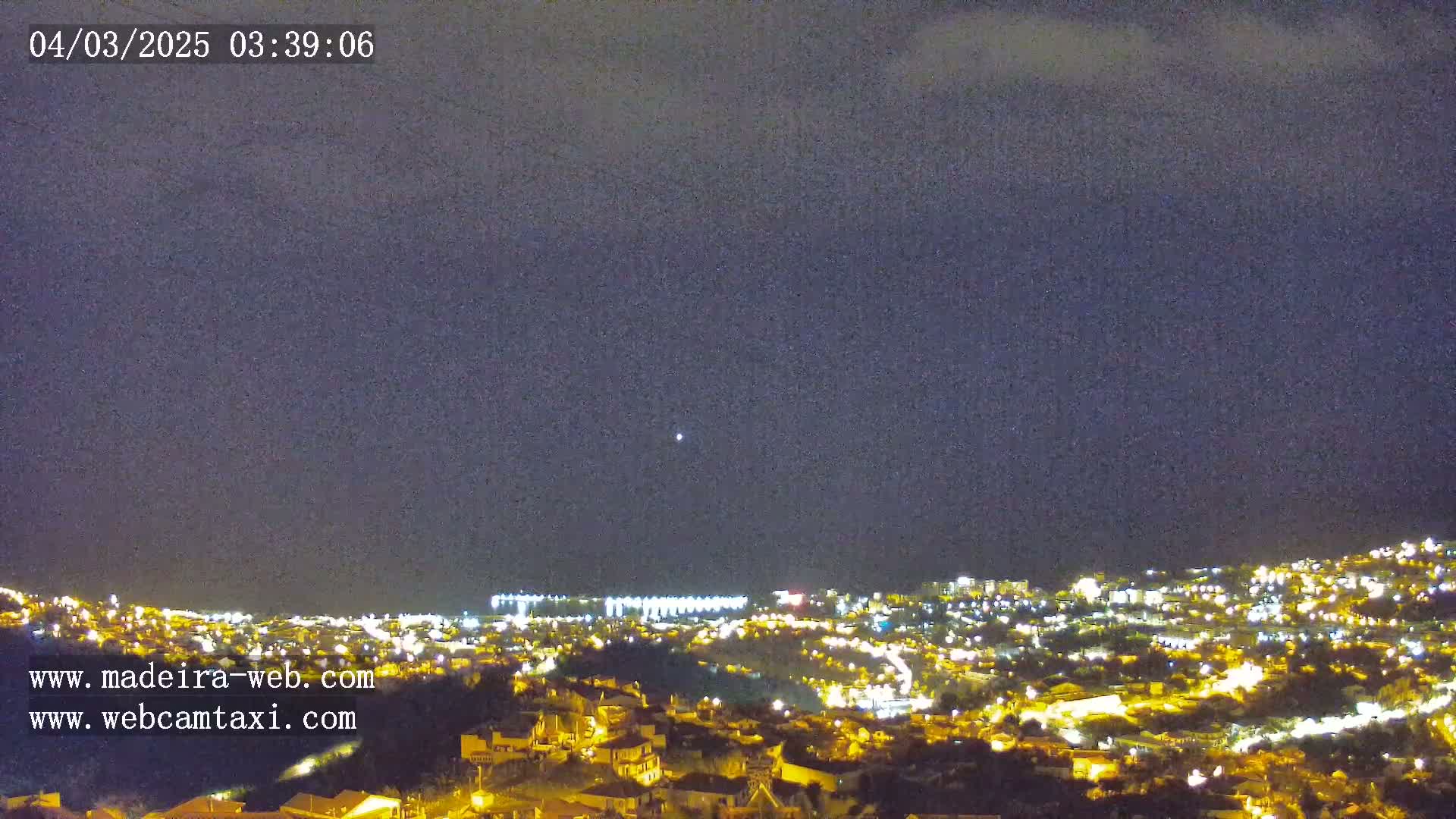 A nighttime view of a city illuminated by numerous lights under a dark, mostly clear sky.