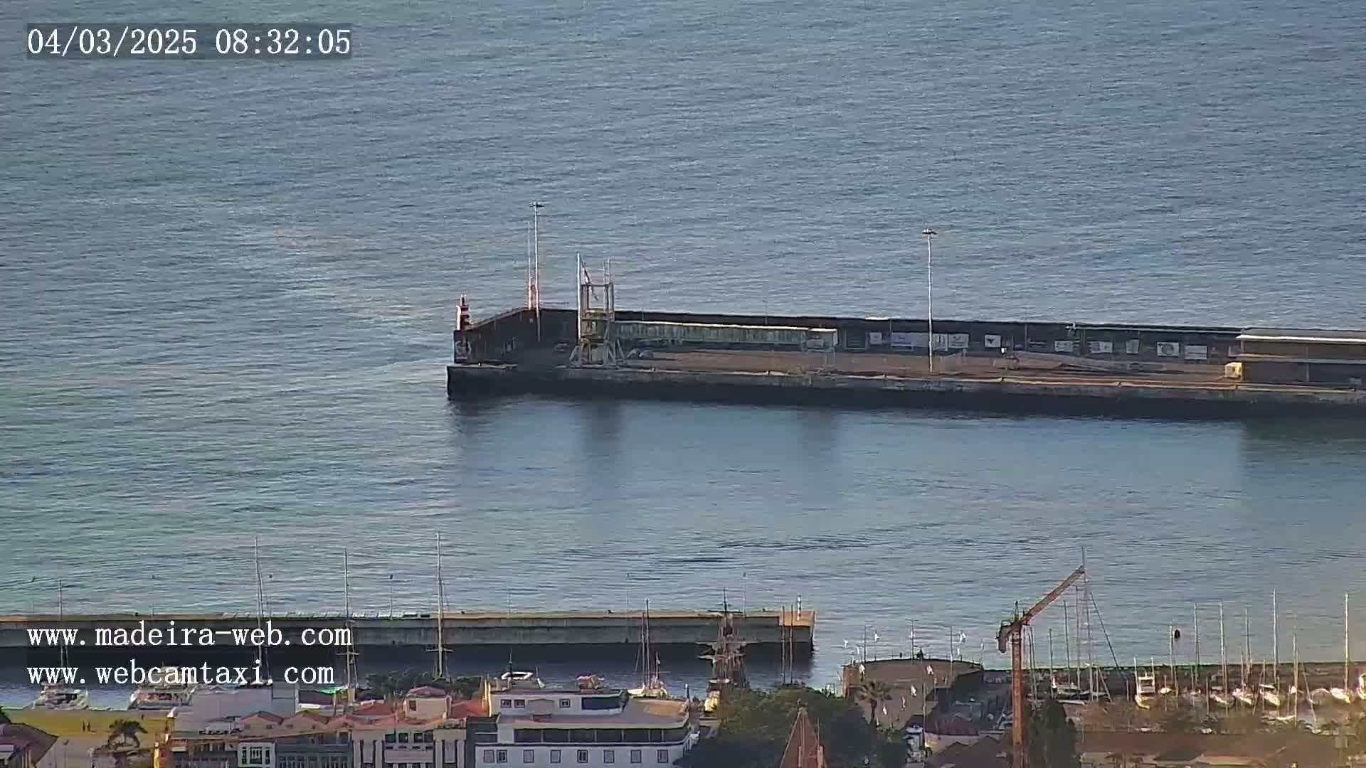 A long pier extends into a calm body of water, with a harbor and town visible in the foreground.