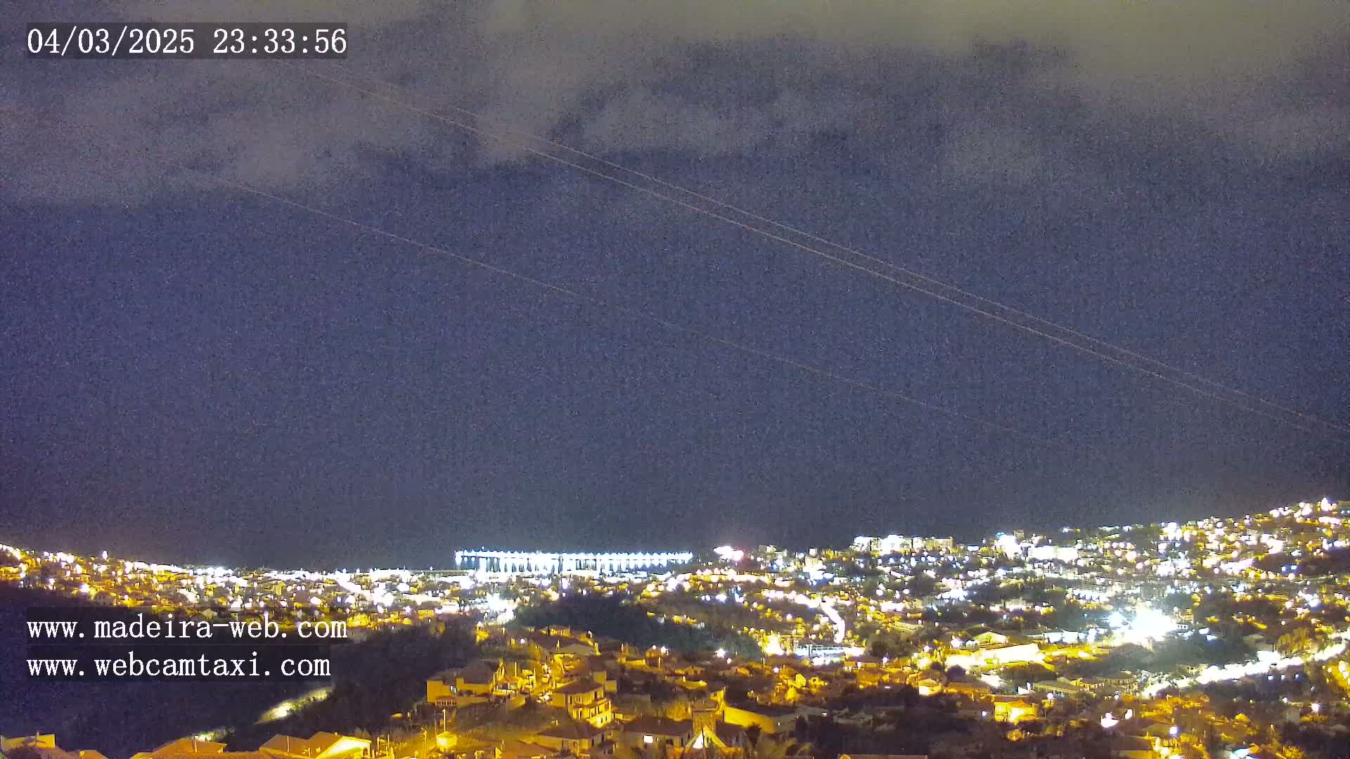 A nighttime view of a city illuminated by lights under a cloudy sky.