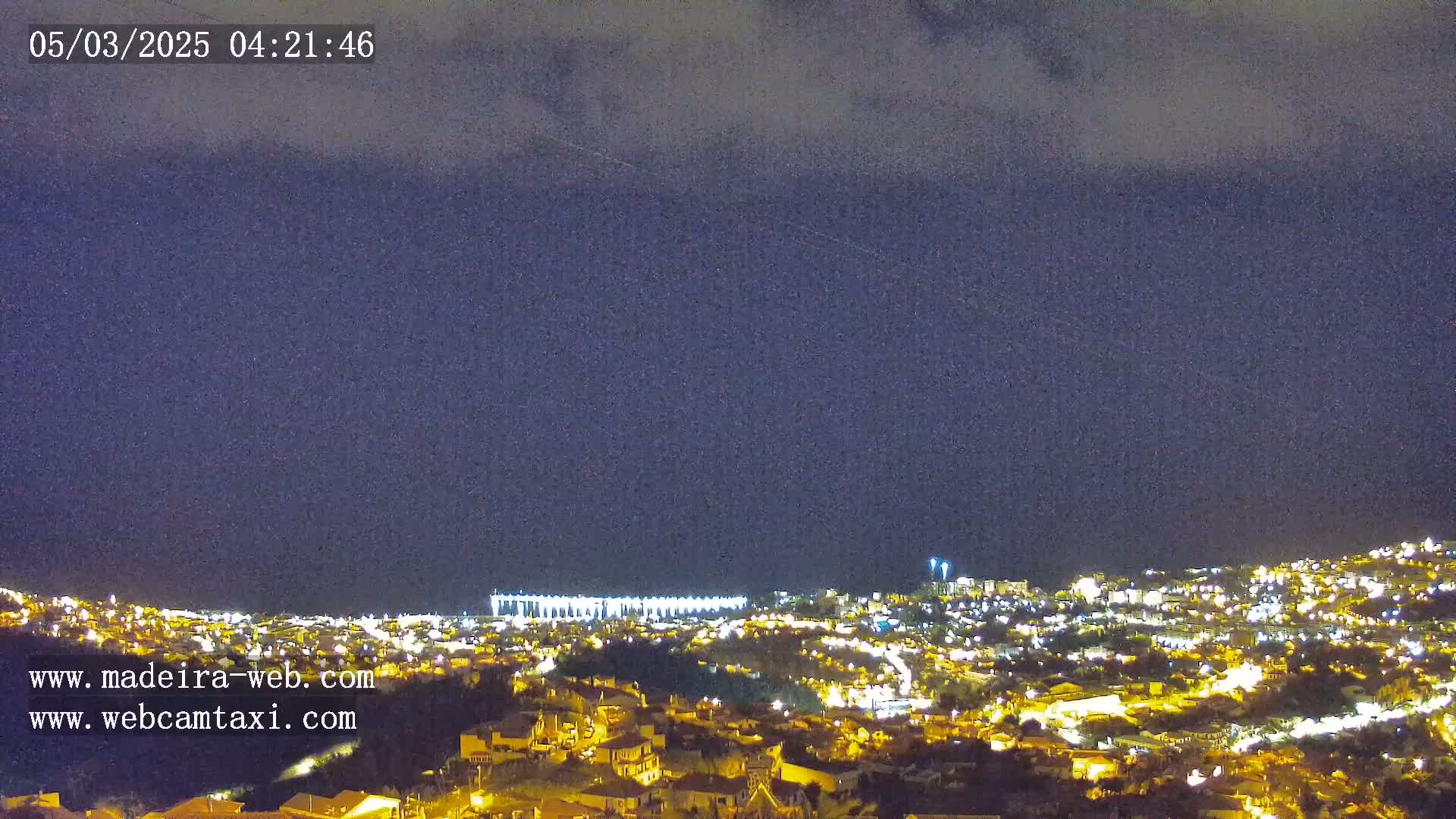 A nighttime view of a city illuminated with small, scattered lights under a dark, cloudy sky.