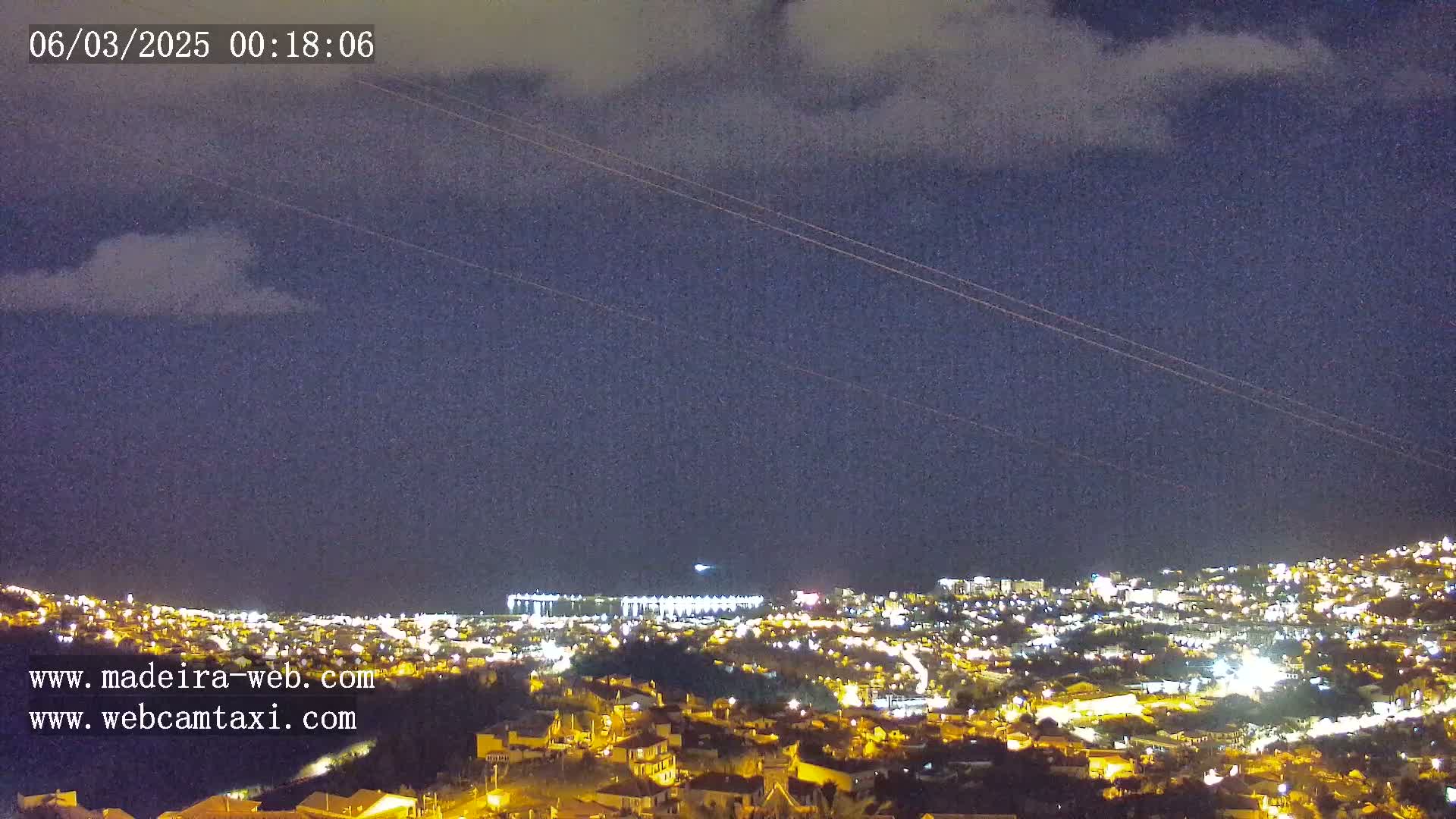 A nighttime view of a city illuminated by lights, situated below a dark sky with a few clouds.