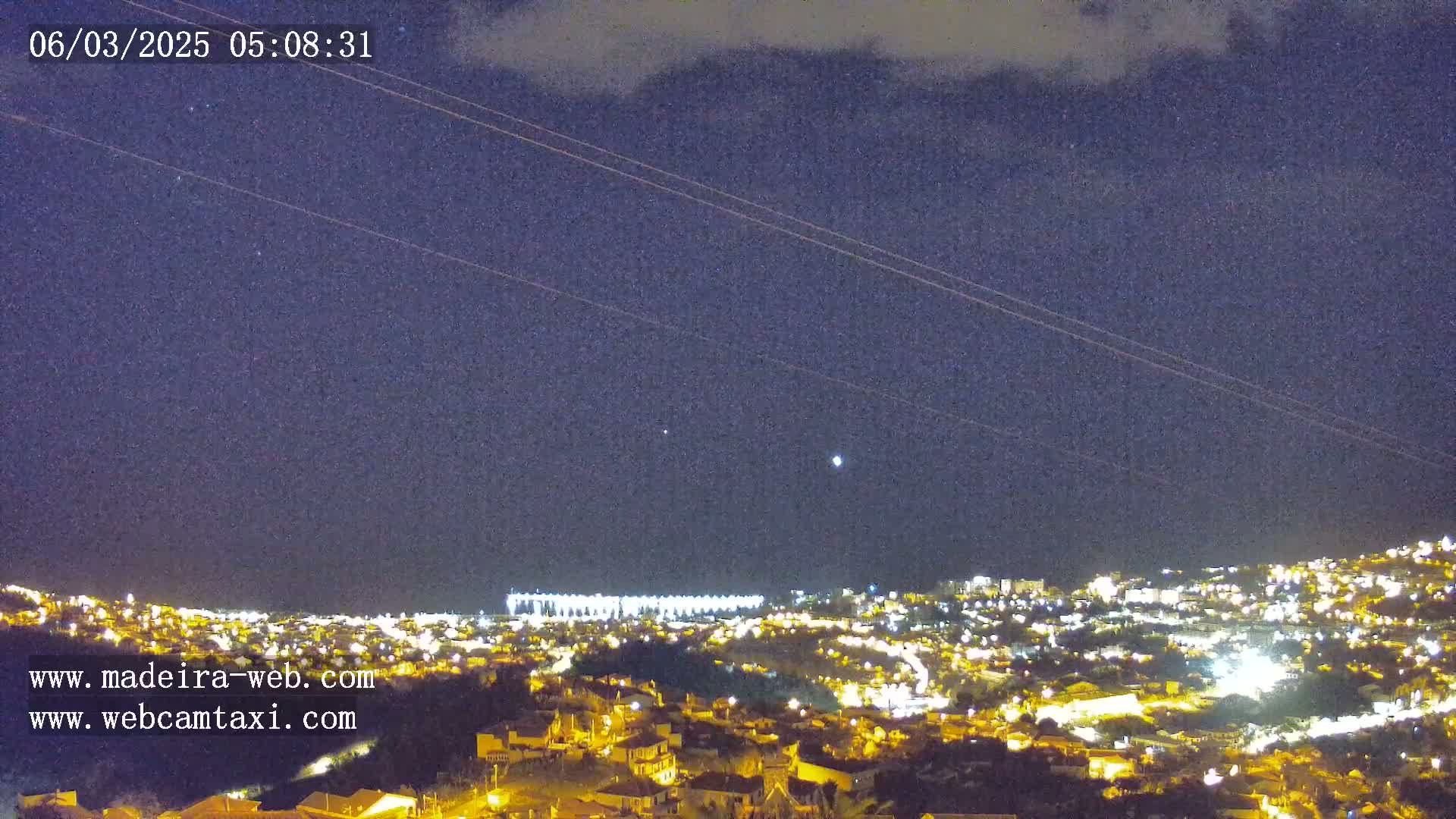 A nighttime view of a city illuminated by lights under a dark, mostly clear sky with a few visible stars.