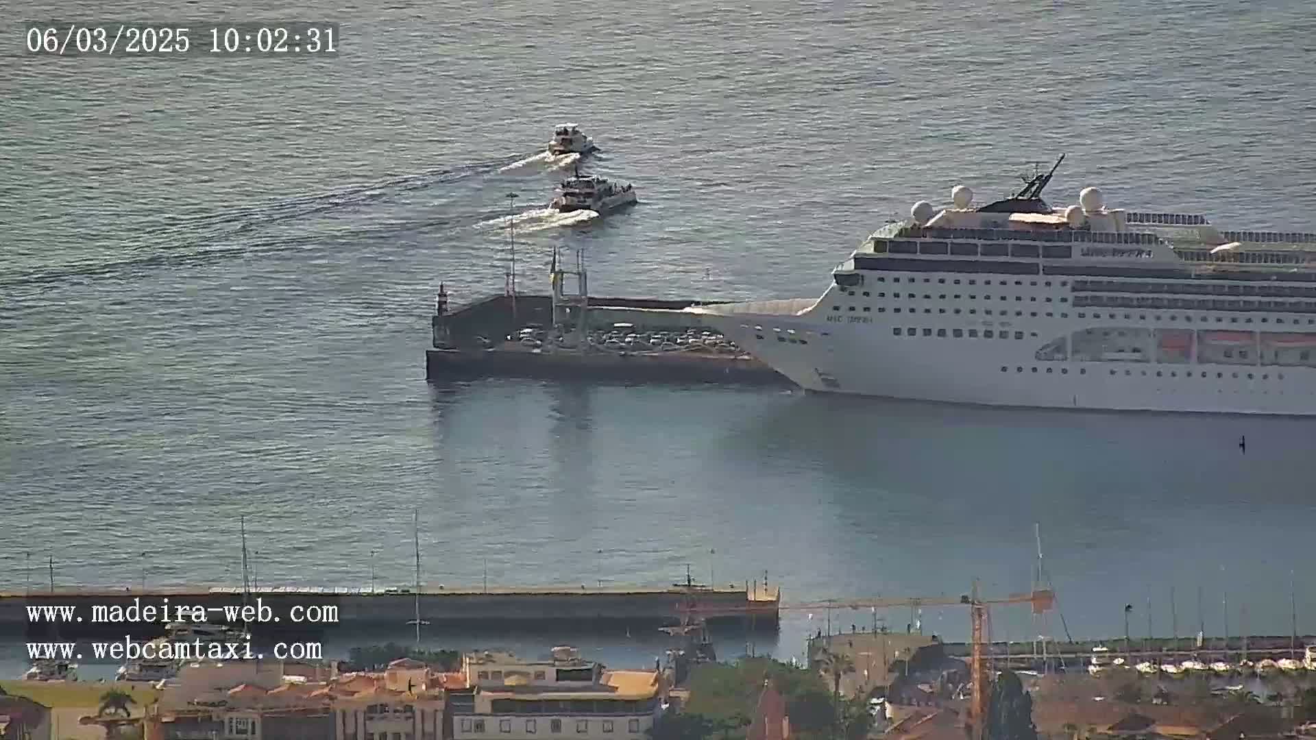 A large cruise ship is docked at a pier, with several smaller boats nearby in calm water.