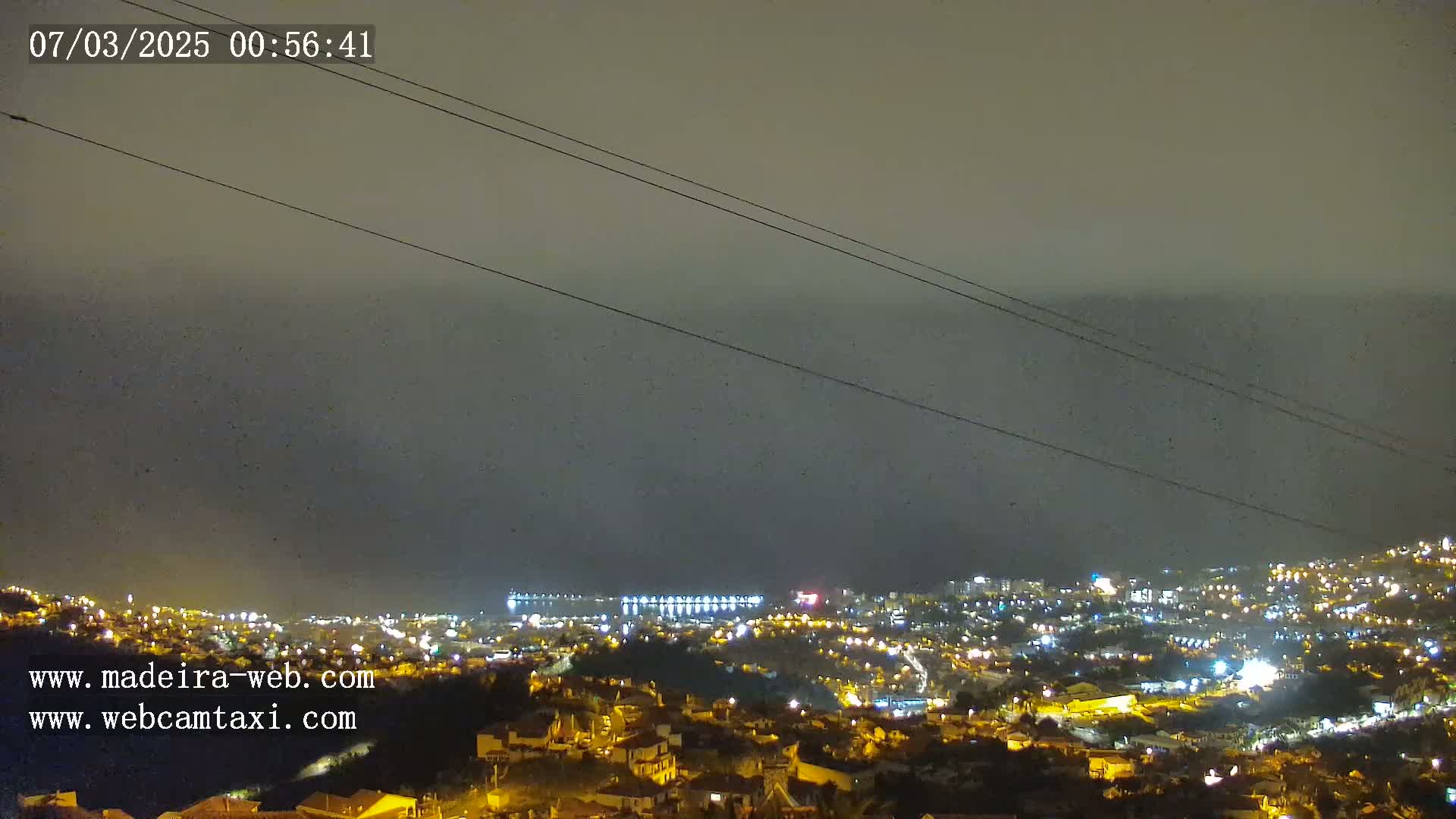 A nighttime view of a coastal city illuminated with lights under a hazy, dark sky.
