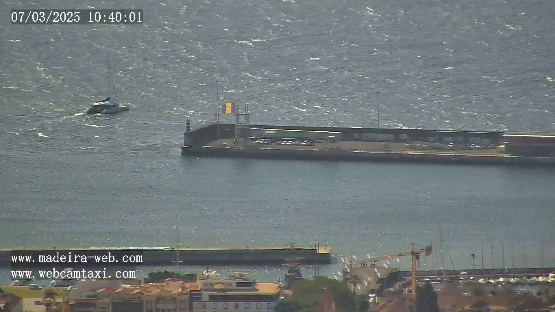 A small boat is in choppy water near a harbor, with buildings and a crane visible in the background.