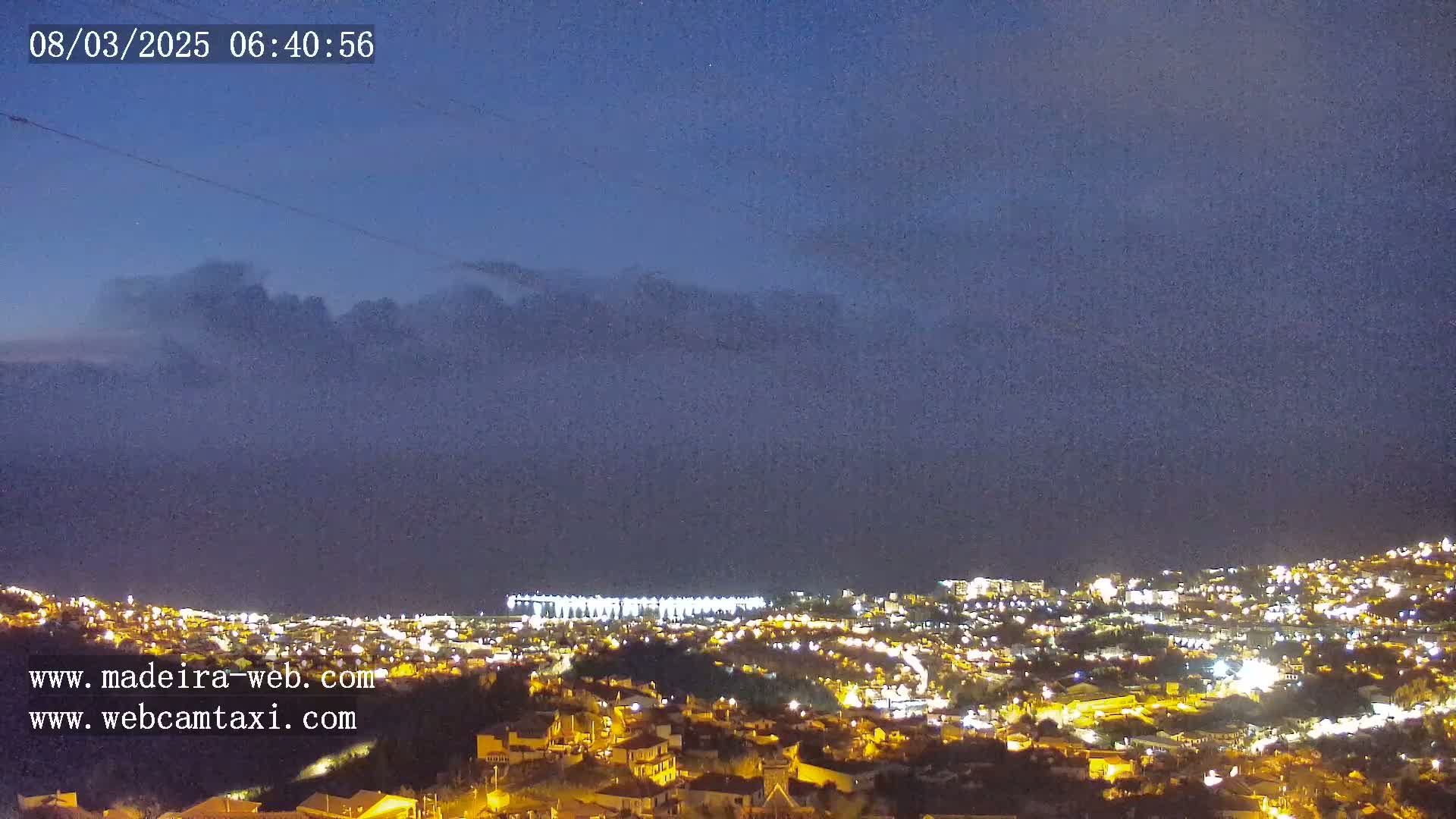 A nighttime view of a city illuminated by lights, under a dark, cloudy sky.