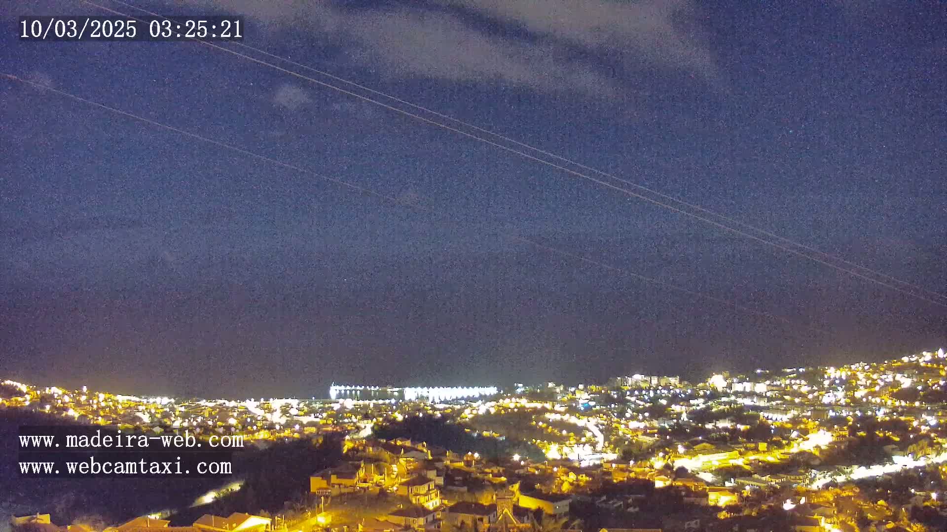 A nighttime view of a city illuminated by lights, situated on a hillside under a mostly clear, dark sky.