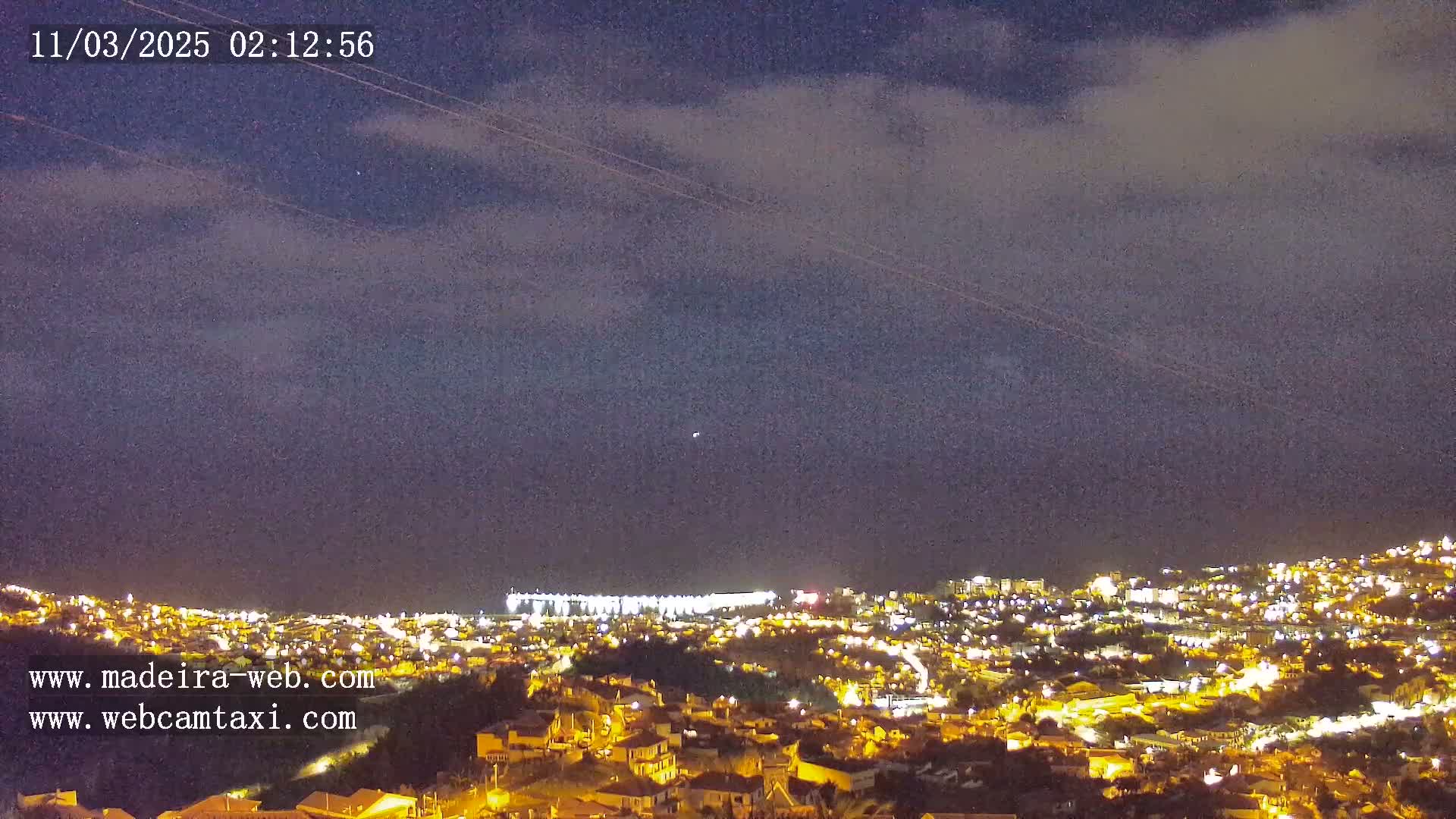 A nighttime view of a city illuminated by lights under a partly cloudy sky.