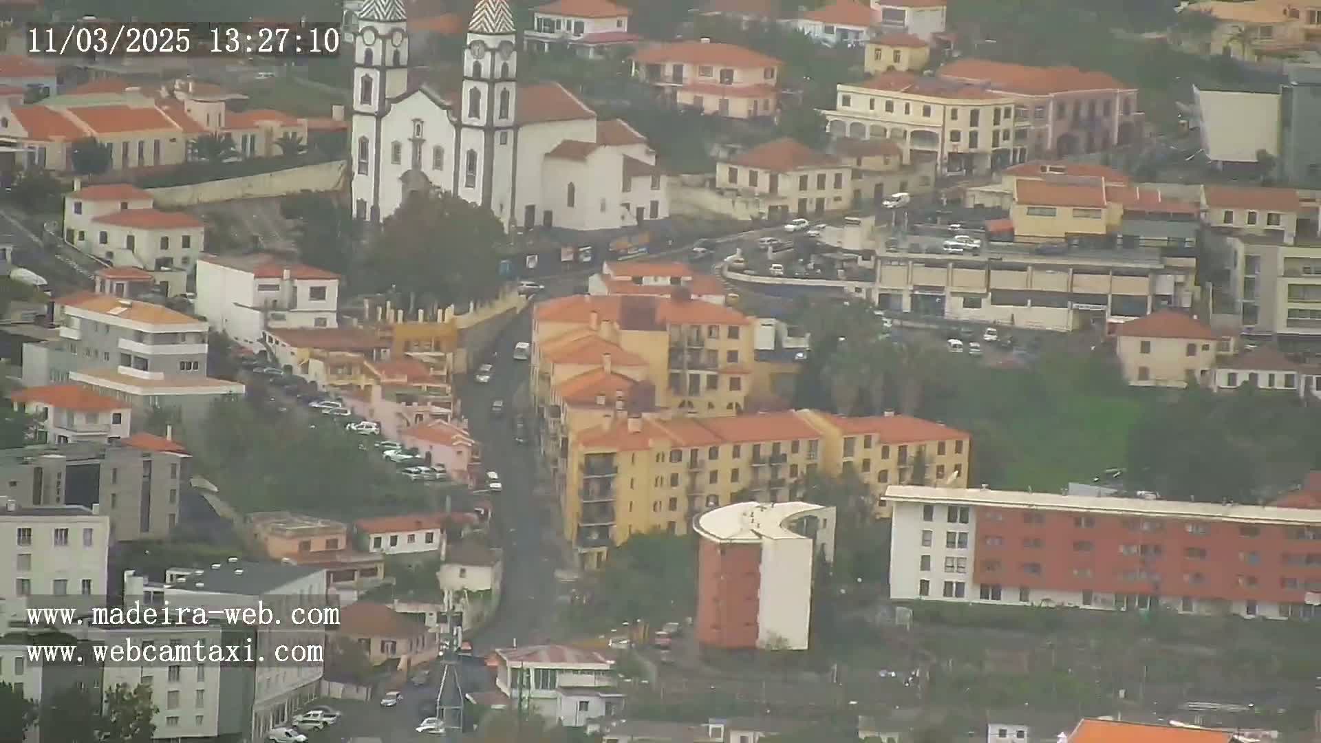 An aerial view of a town on a cloudy day, showing a church with twin towers and many low-rise buildings.