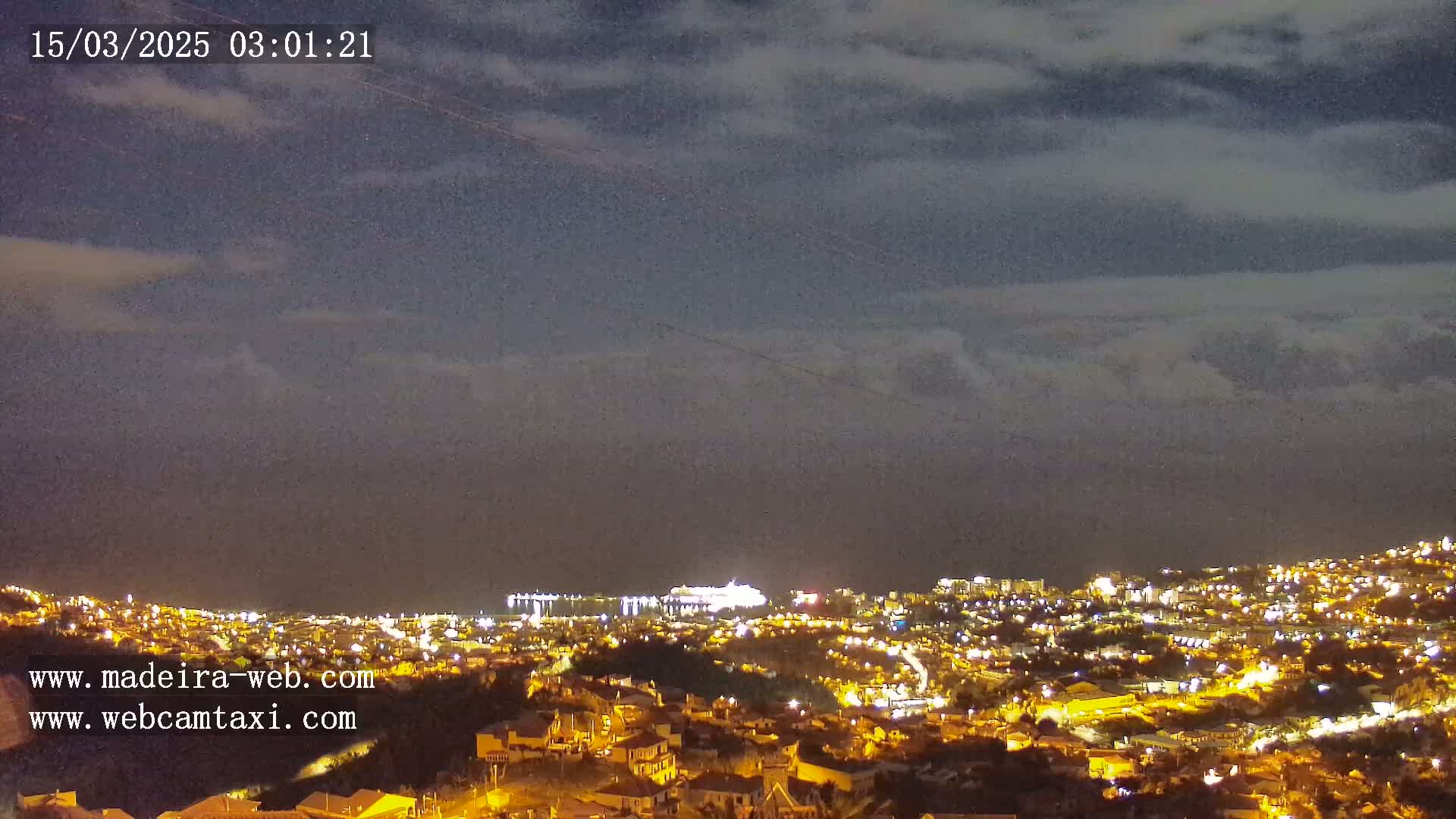 A nighttime view of a city illuminated by lights, under a cloudy sky.