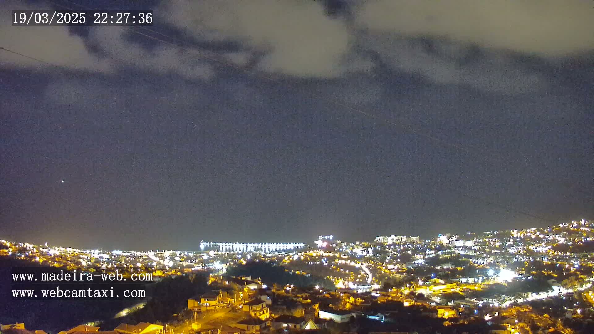 A nighttime view of a city illuminated by lights under a mostly cloudy sky.