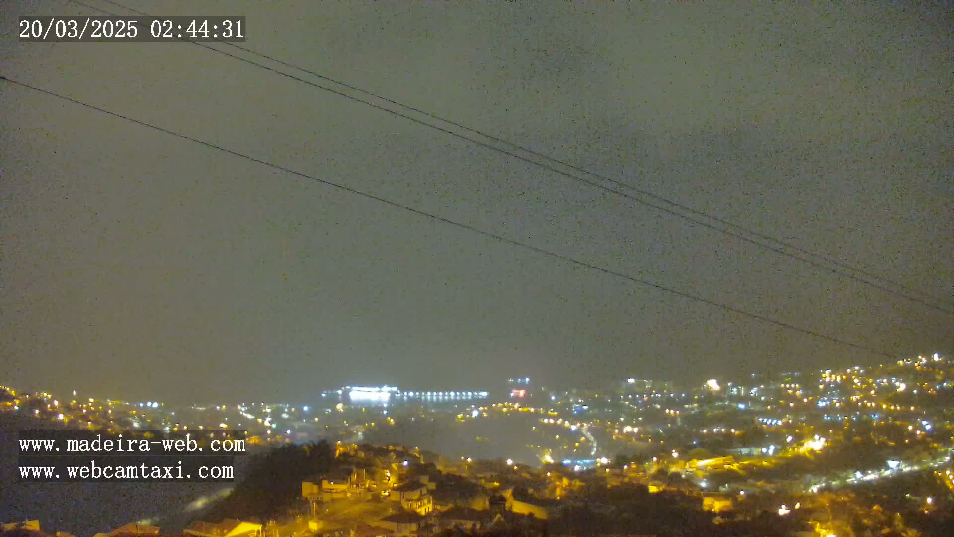 A nighttime, hazy view of a city illuminated by streetlights, with power lines in the foreground.