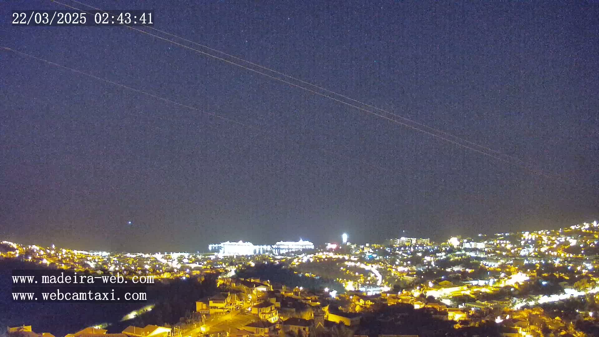 A nighttime, clear-sky view of a city illuminated with many lights, situated on a hillside overlooking a body of water.
