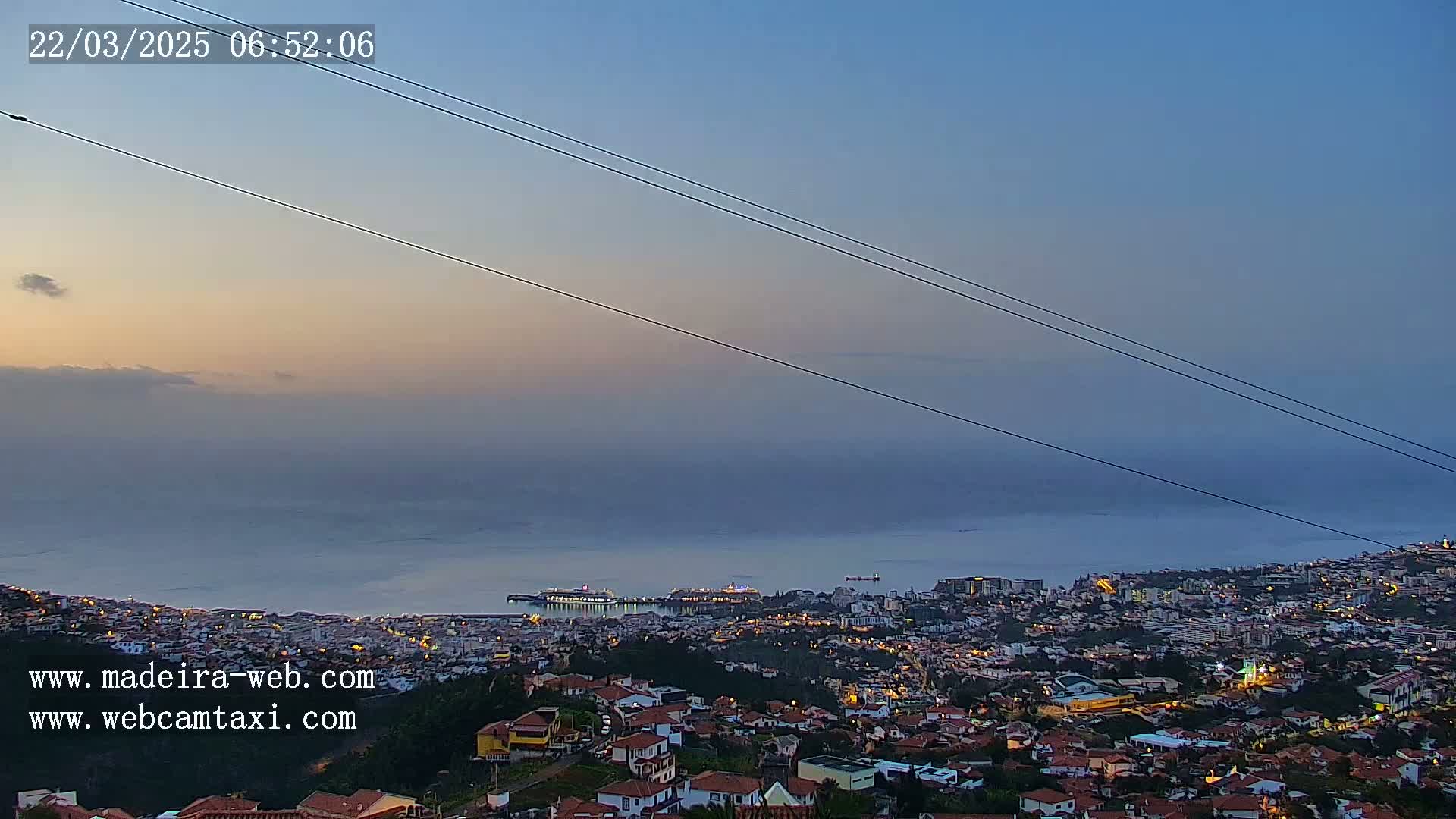 A coastal town at dawn is partially shrouded in fog, with a cruise ship visible in the harbor.