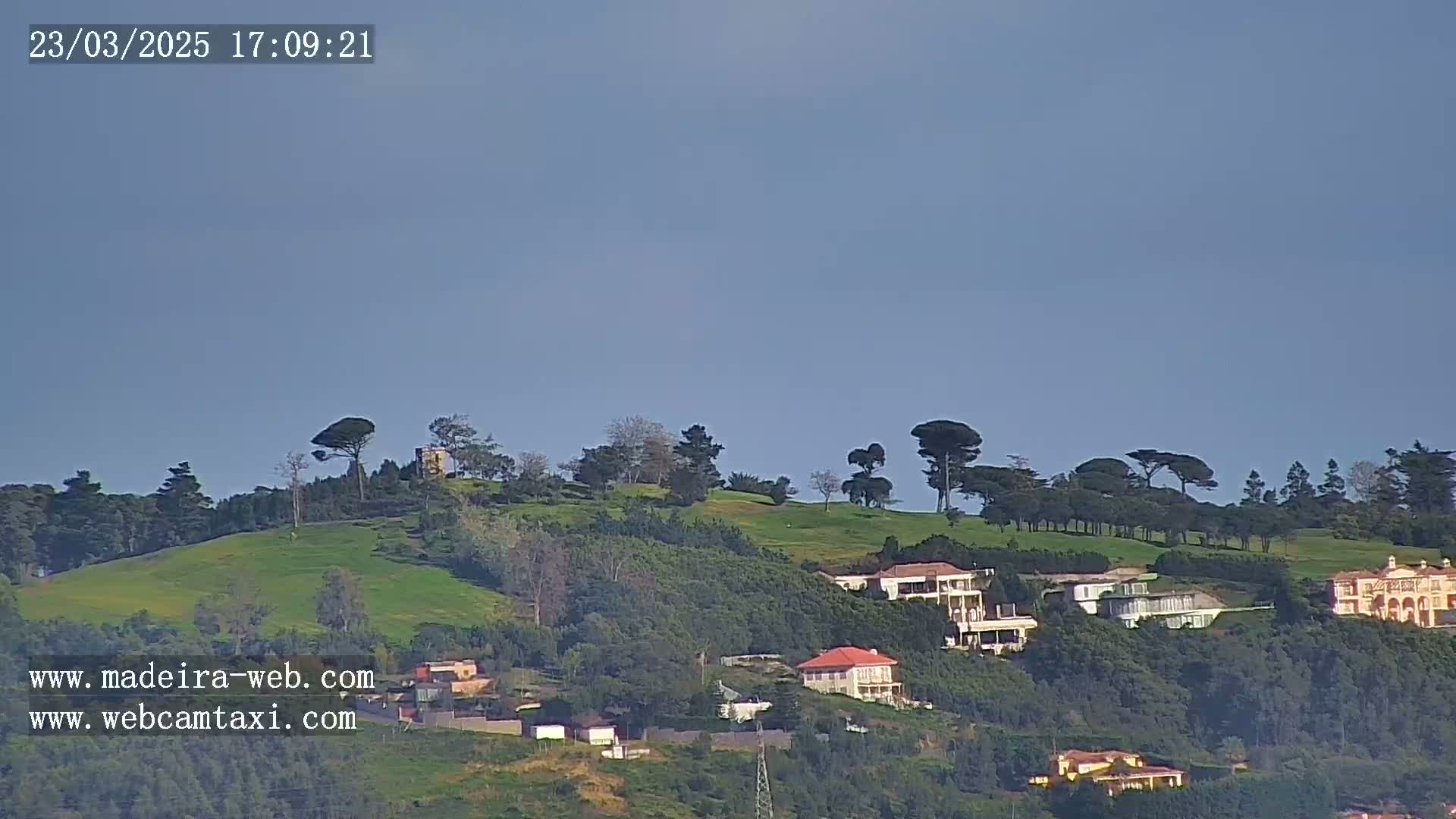 A grassy hillside dotted with trees and houses is visible under a clear, light-blue sky.