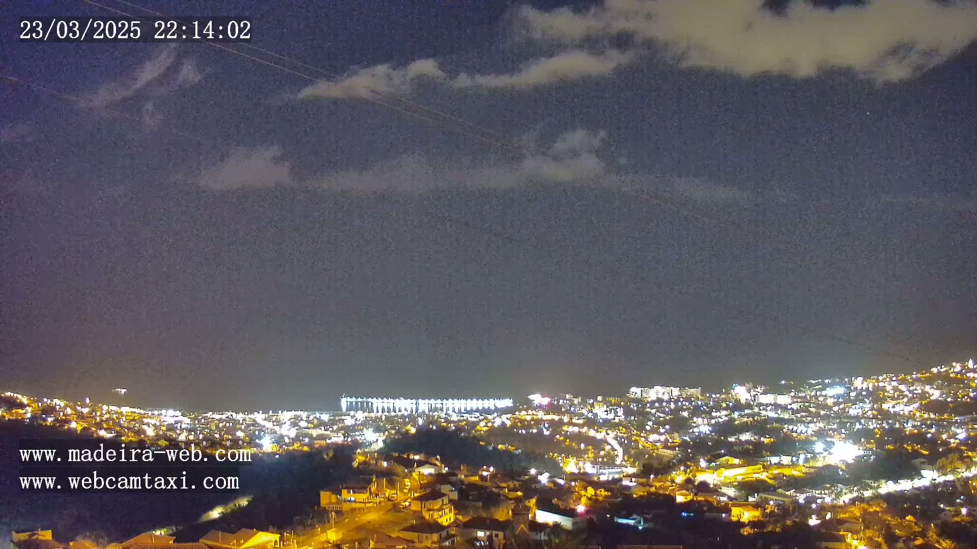 A nighttime view of a city illuminated with streetlights under a partly cloudy sky.