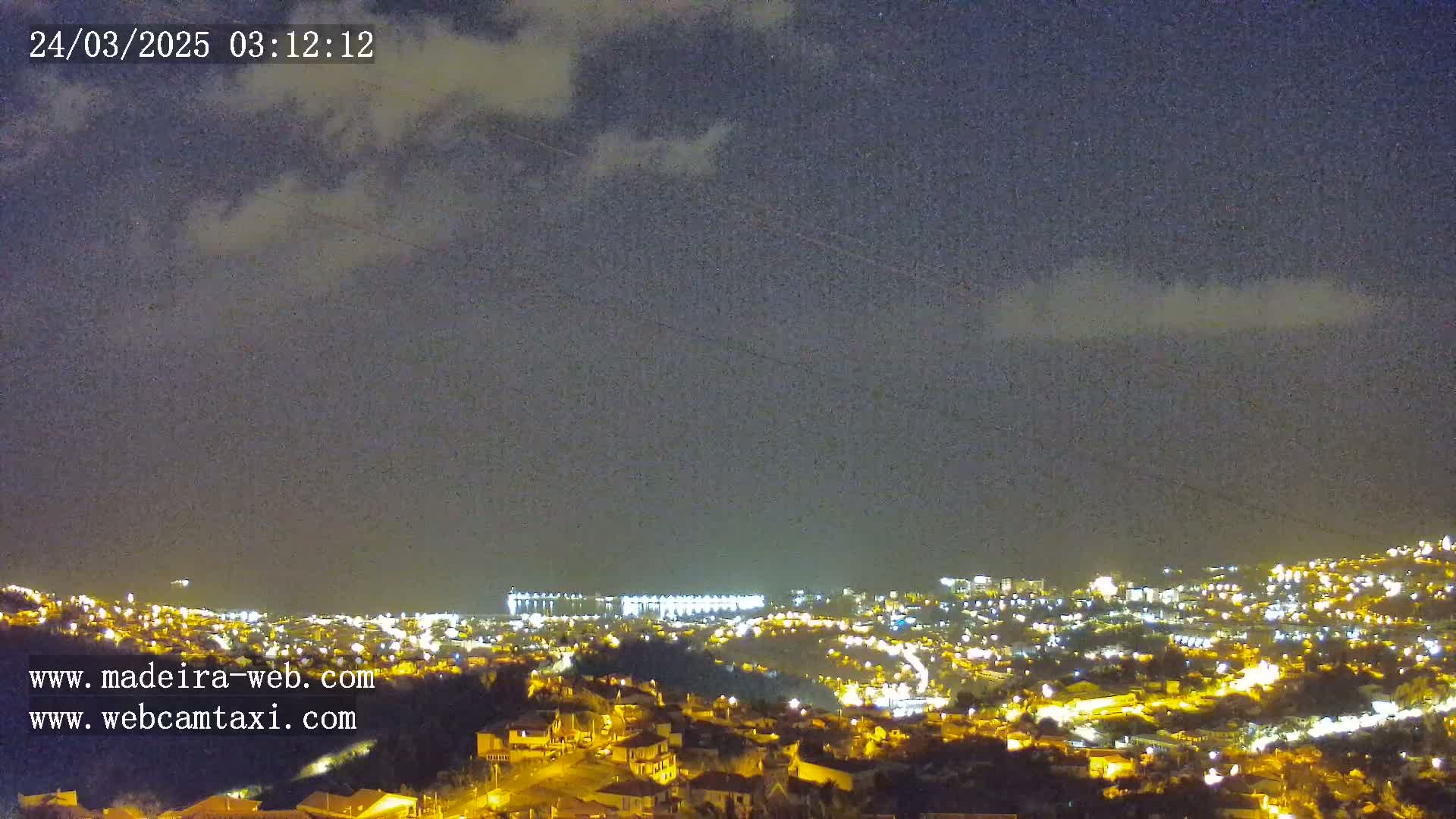 A nighttime view of a city illuminated by lights under a partly cloudy sky.