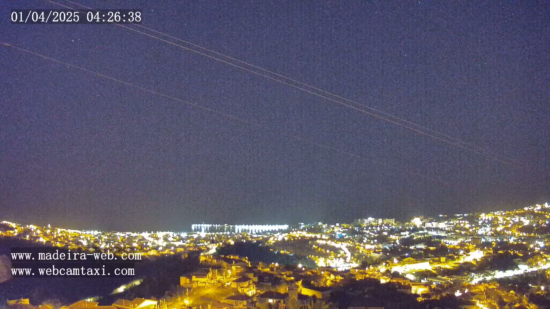 A nighttime, clear-sky view of a city illuminated by many lights, extending to a distant shoreline.