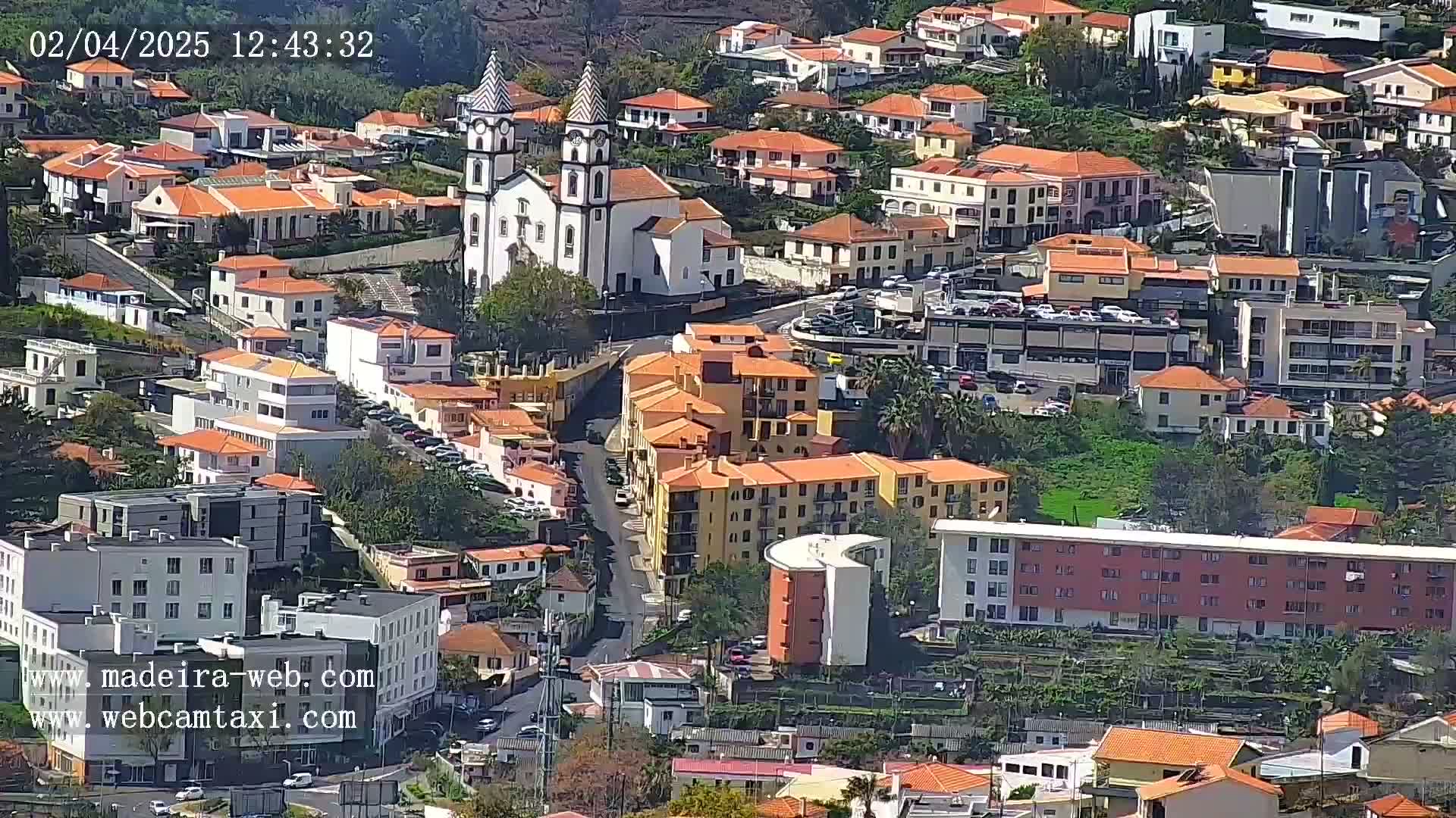 A sunny aerial view of a town shows many low-rise buildings clustered around a large church with twin bell towers.