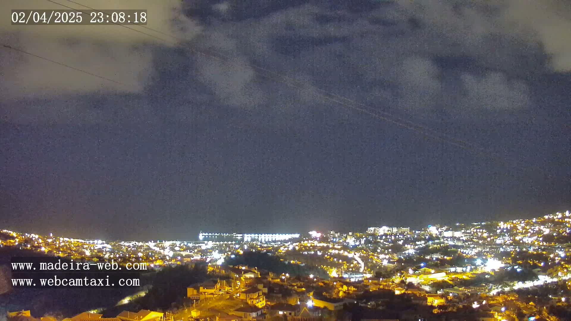 A nighttime view of a city illuminated by lights under a partly cloudy sky.