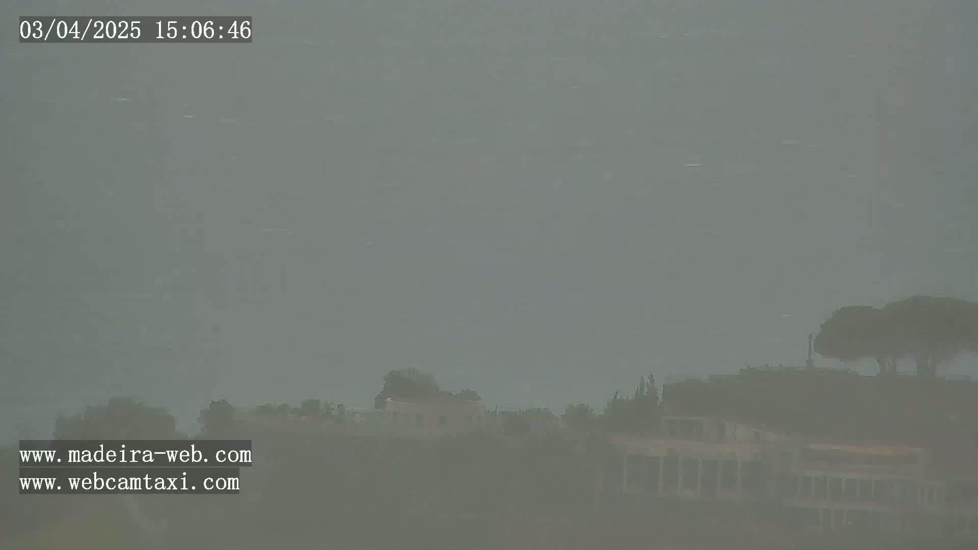 A hazy, overcast scene shows indistinct buildings and trees on a hillside.