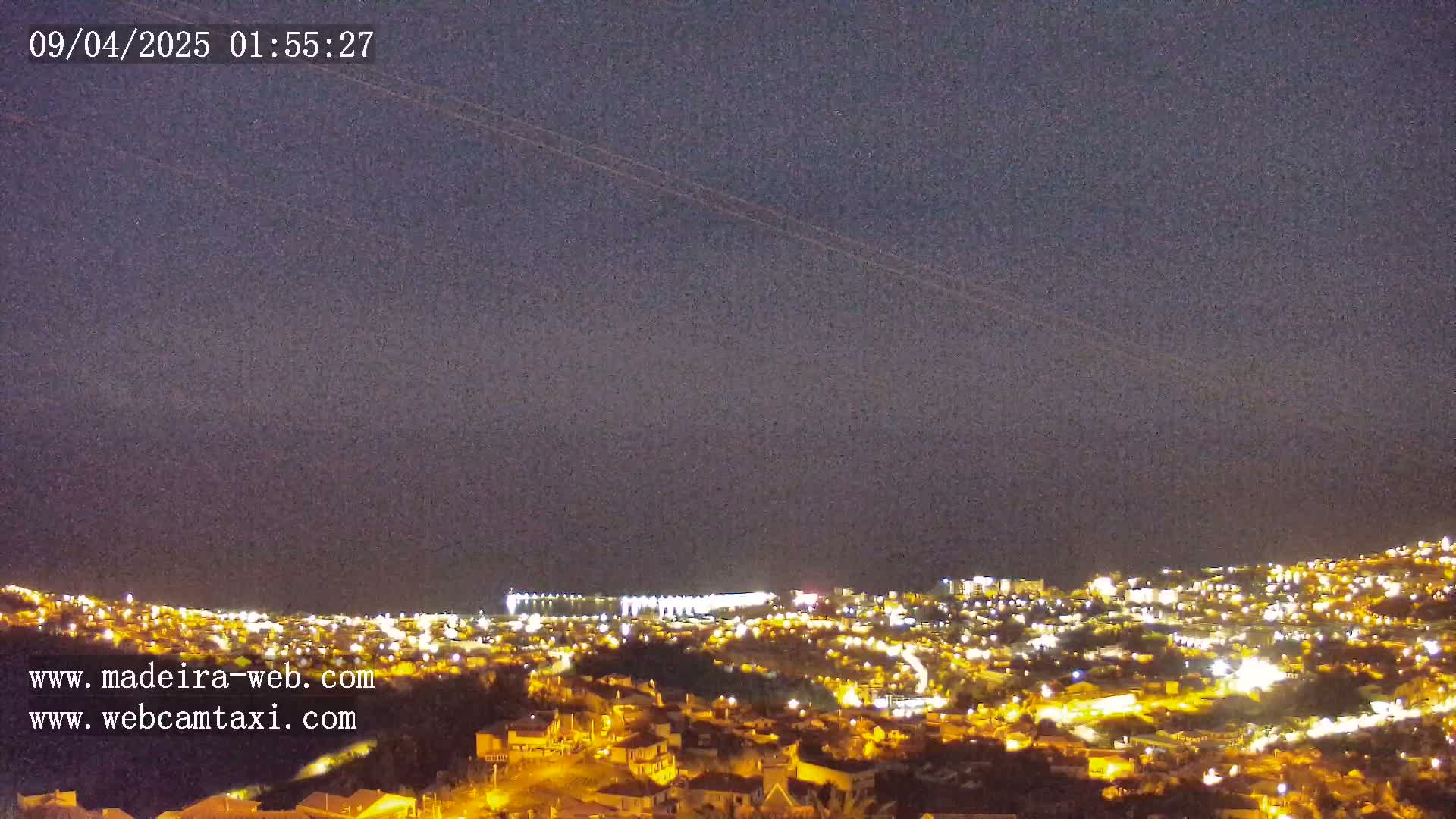A nighttime view of a coastal city illuminated with lights, under a clear, dark sky.