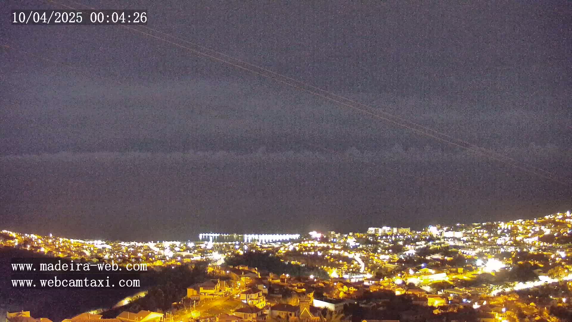 A nighttime view of a city illuminated by lights under a mostly cloudy sky.