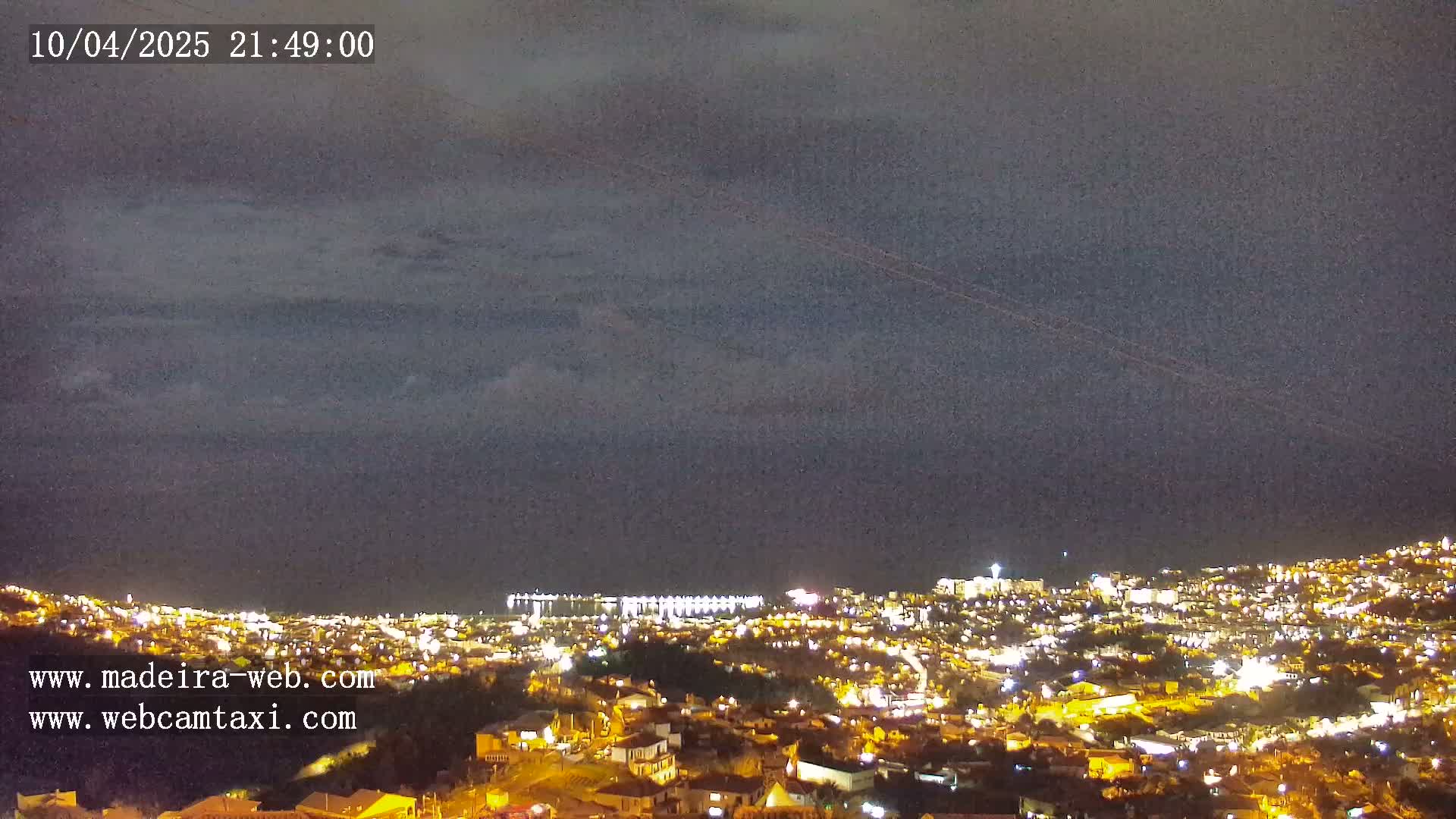 A nighttime view of a city illuminated by lights, under a dark, cloudy sky.