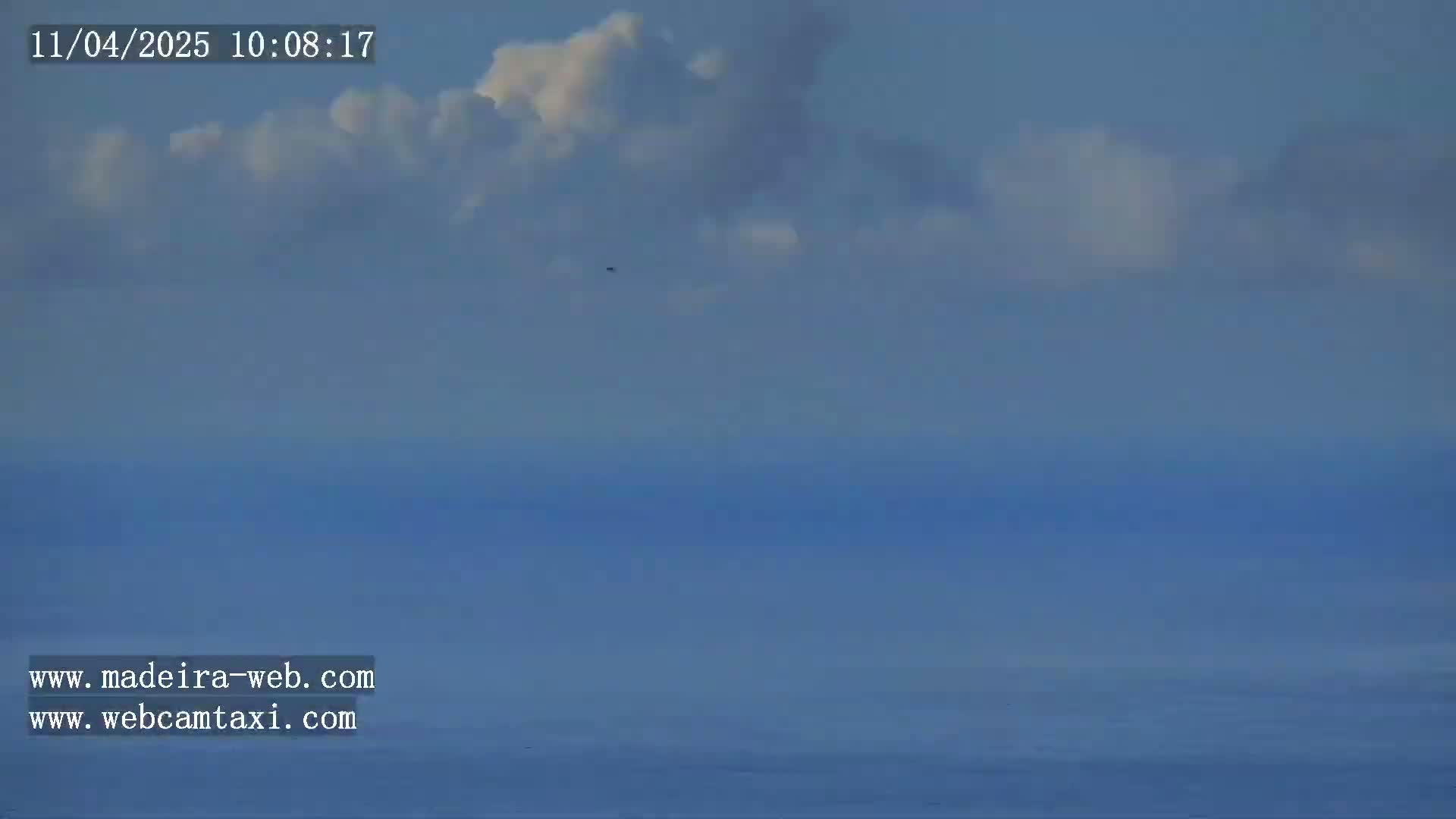 A mostly clear sky with a few fluffy white clouds above a calm, blue ocean.