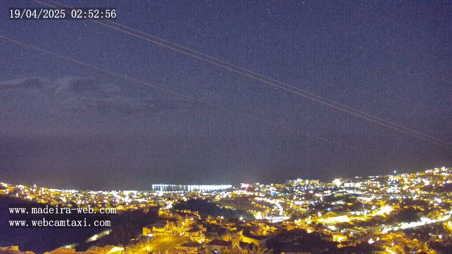 A nighttime view of a city illuminated by lights under a mostly clear, dark sky with a few faint clouds.
