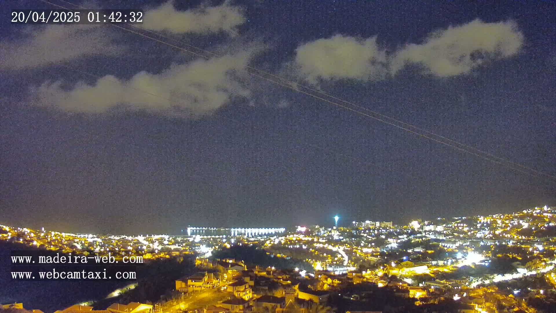 A nighttime view of a city illuminated by lights under a partly cloudy sky.