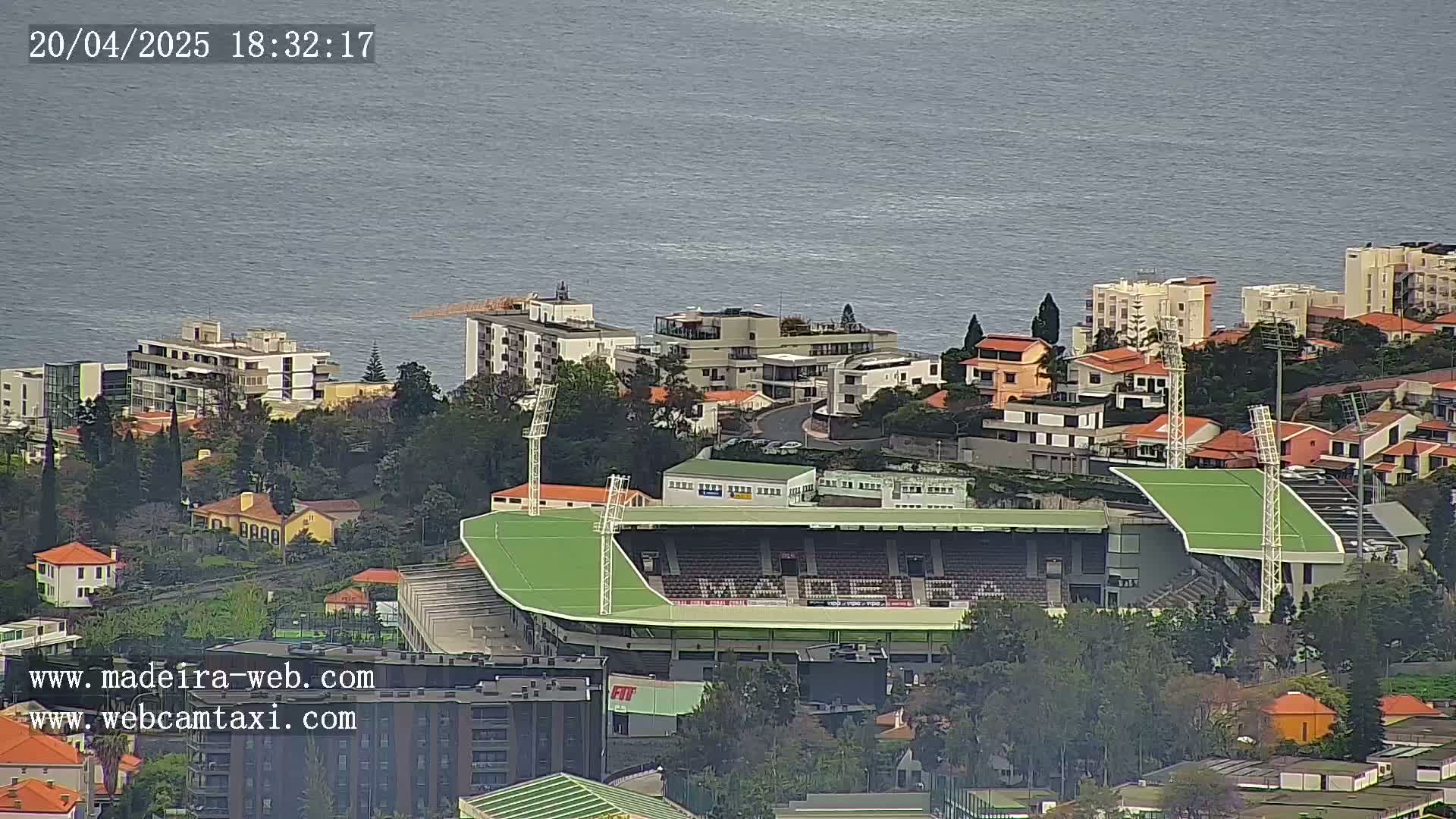 An aerial view shows a green soccer stadium nestled among residential buildings overlooking a calm body of water.