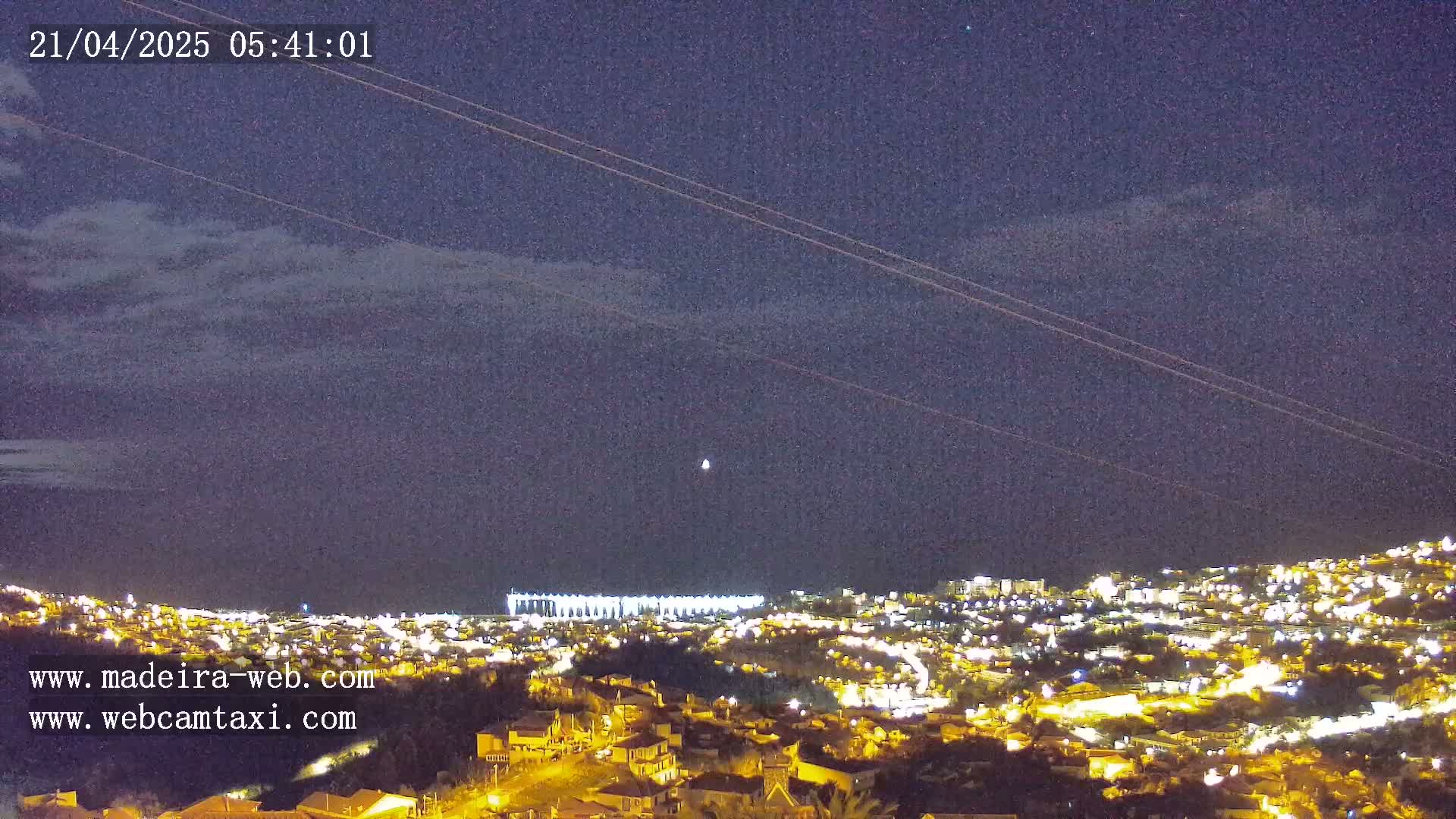 A nighttime view of a city illuminated by lights under a partly cloudy sky.