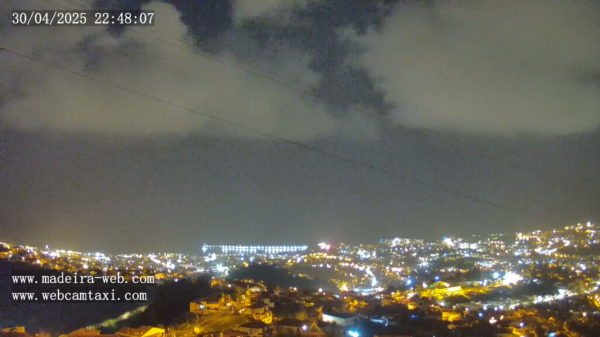 A nighttime view of a city illuminated by lights under a cloudy sky.