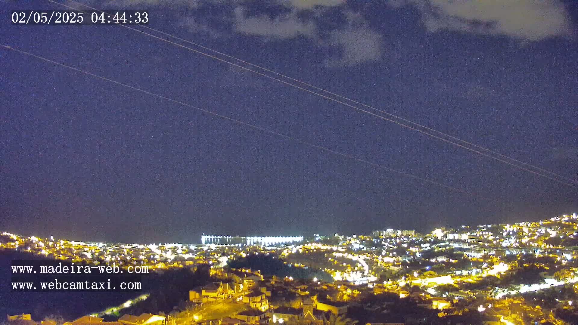 A nighttime view of a city illuminated by many lights under a mostly clear, dark-blue sky.