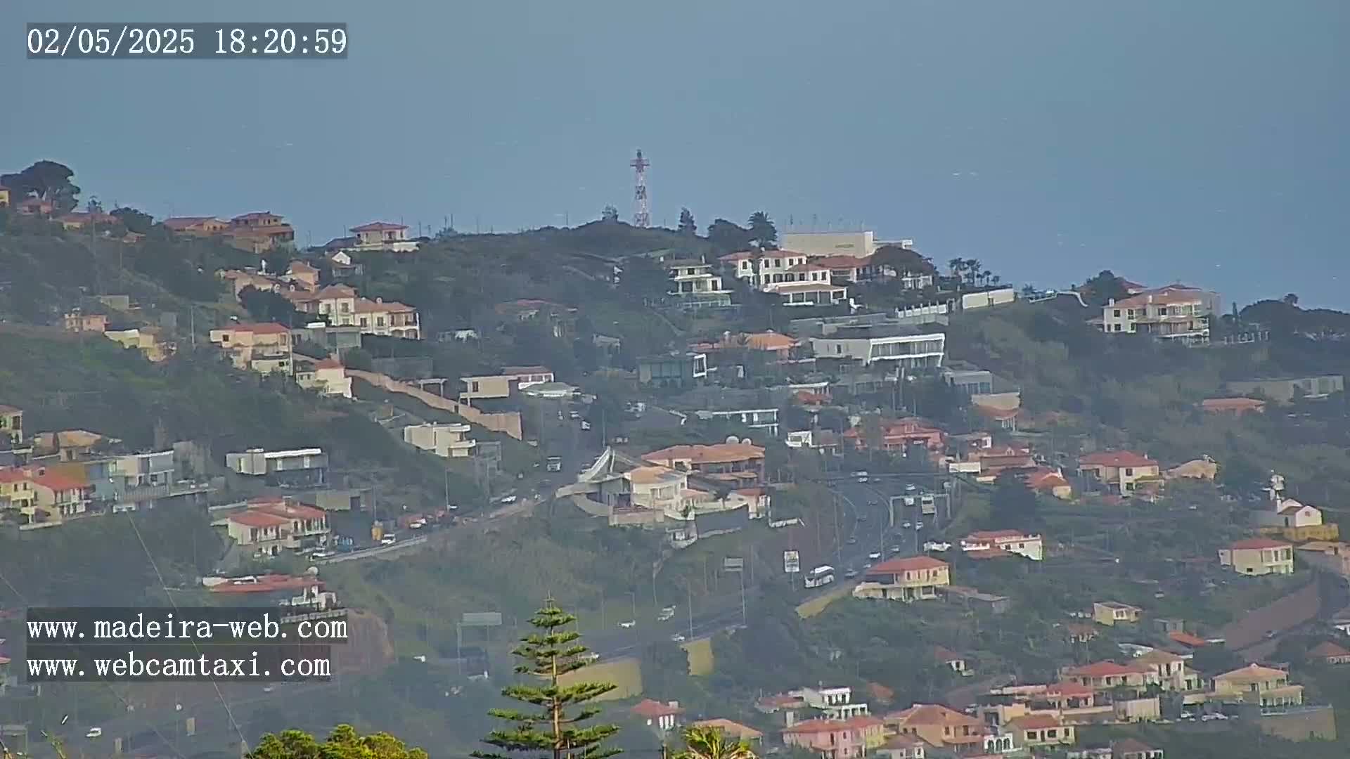 A hazy view shows a hillside covered in houses and a communication tower, overlooking a body of water.