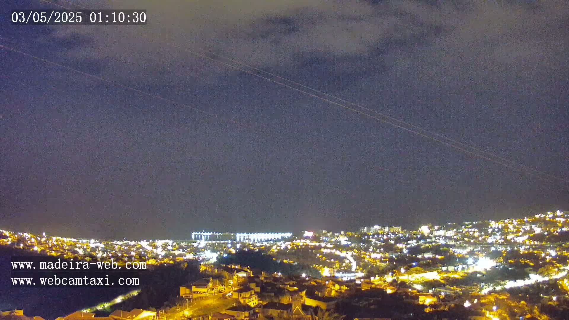 A nighttime view of a city illuminated by lights under a mostly cloudy sky.