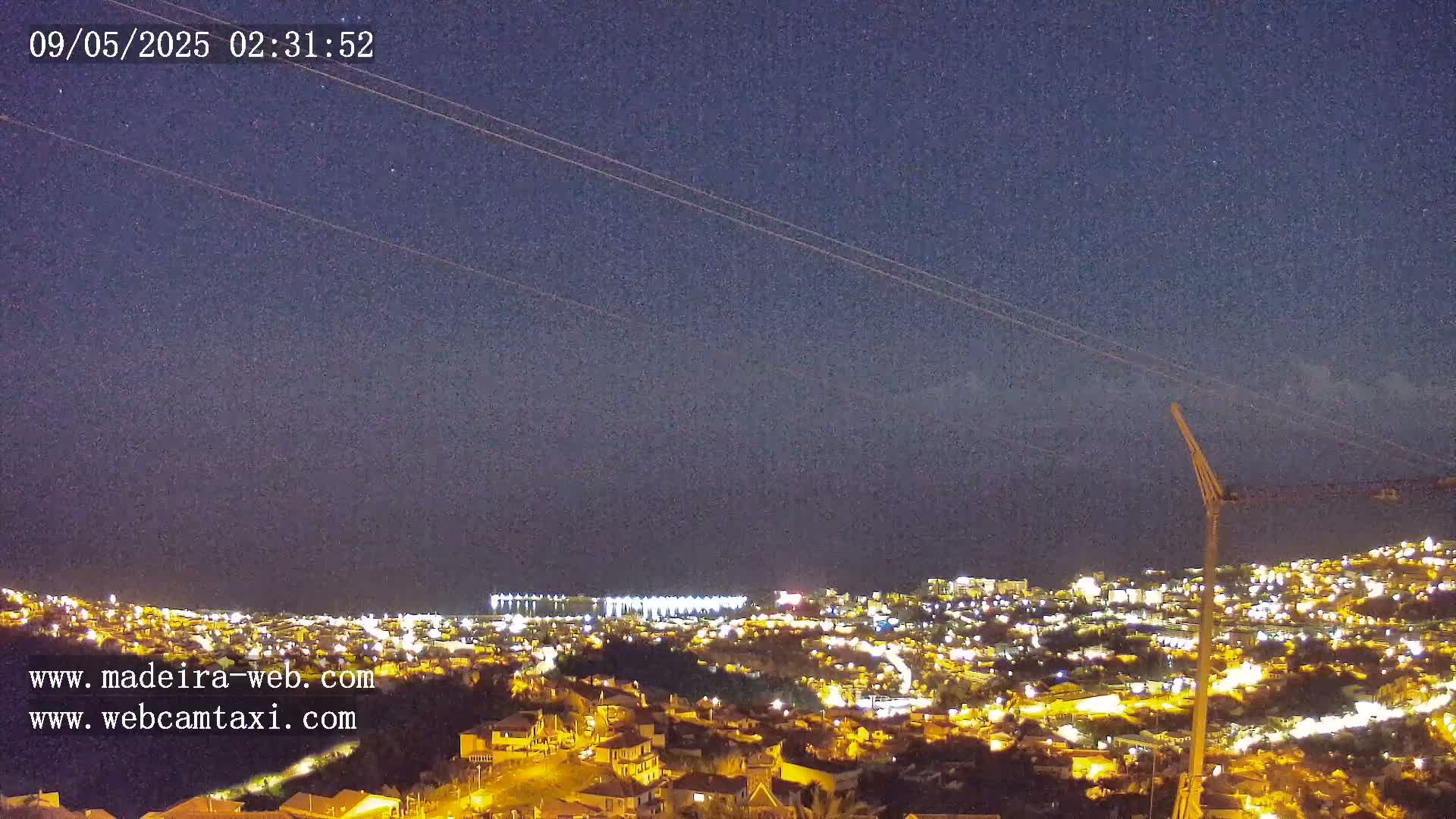 A nighttime view of a city illuminated by lights, extending to a dark ocean under a mostly clear, starry sky.