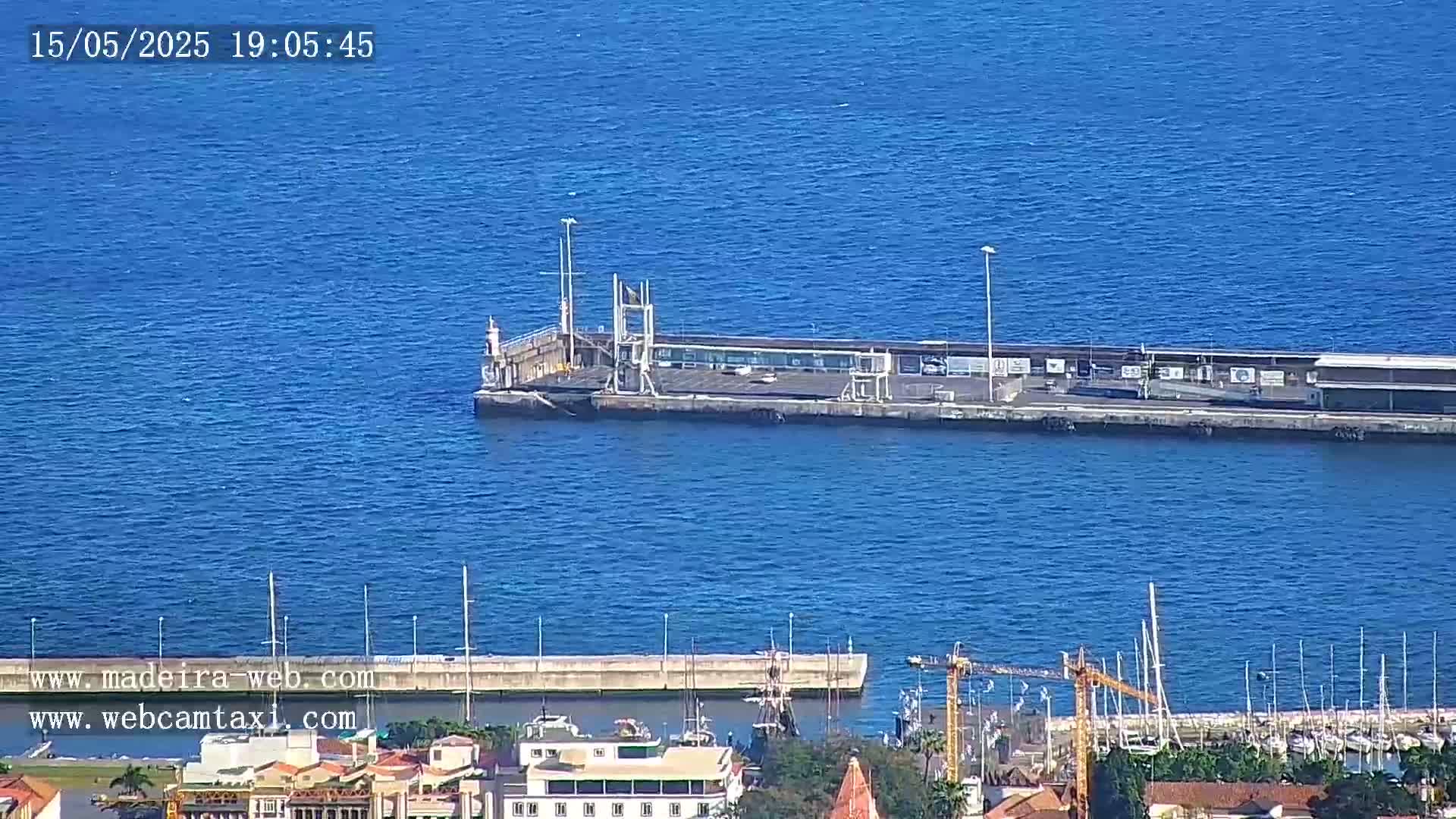 A long pier extends into a calm, blue ocean, with a marina and town visible in the foreground.