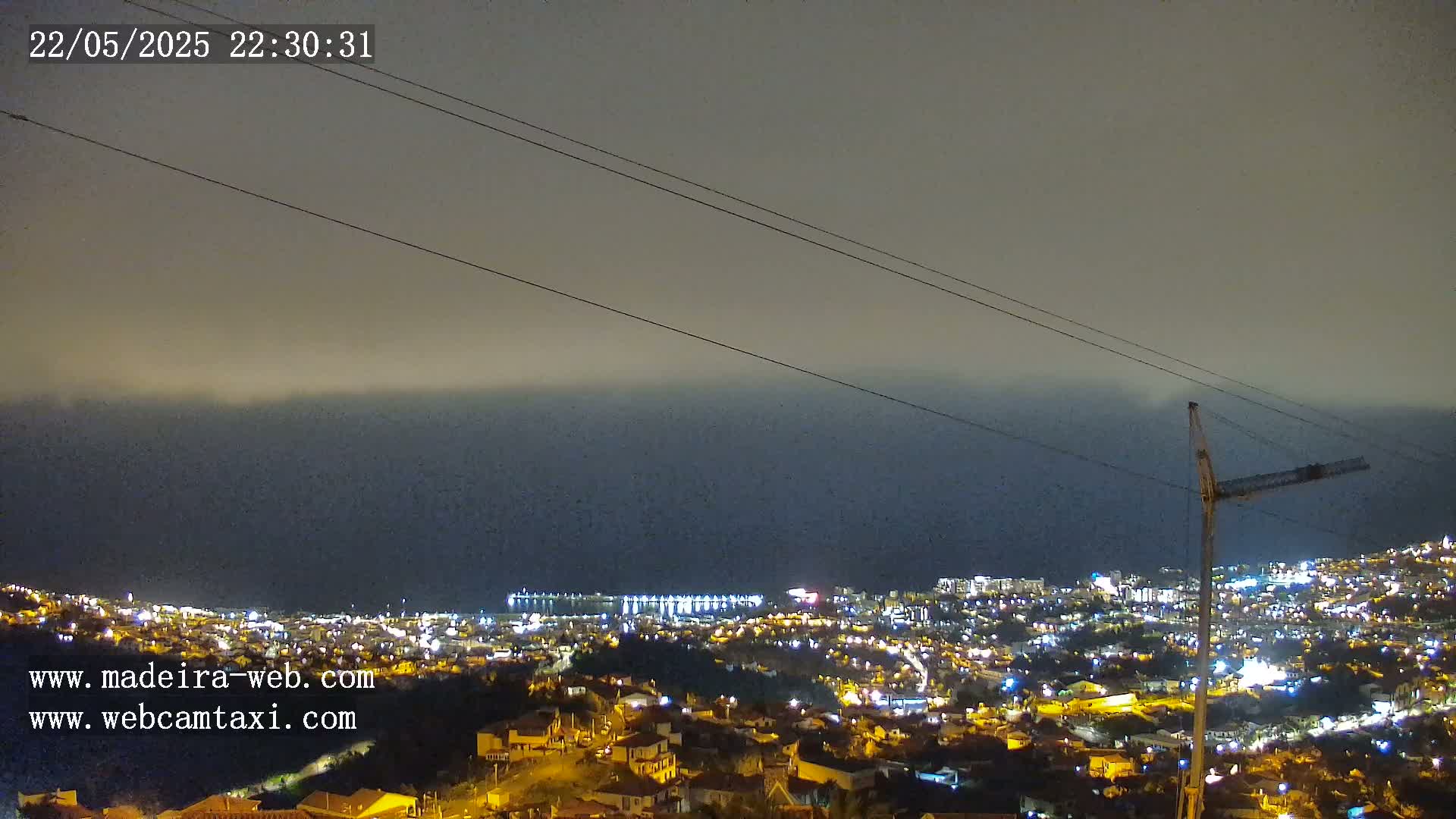A nighttime view of a coastal city illuminated with lights, under a hazy sky.