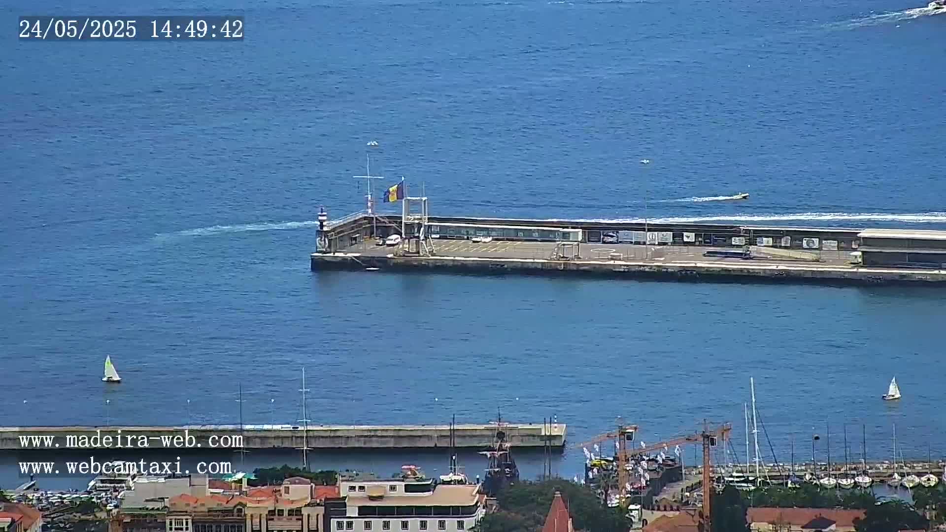 A harbor with a long pier, several boats, and calm blue water under a sunny sky.