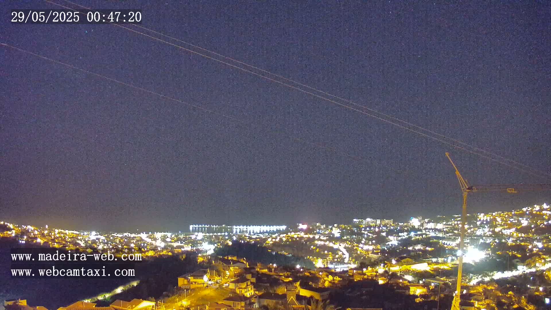 A nighttime view of a city illuminated by lights under a clear, dark sky, with a construction crane visible in the foreground.