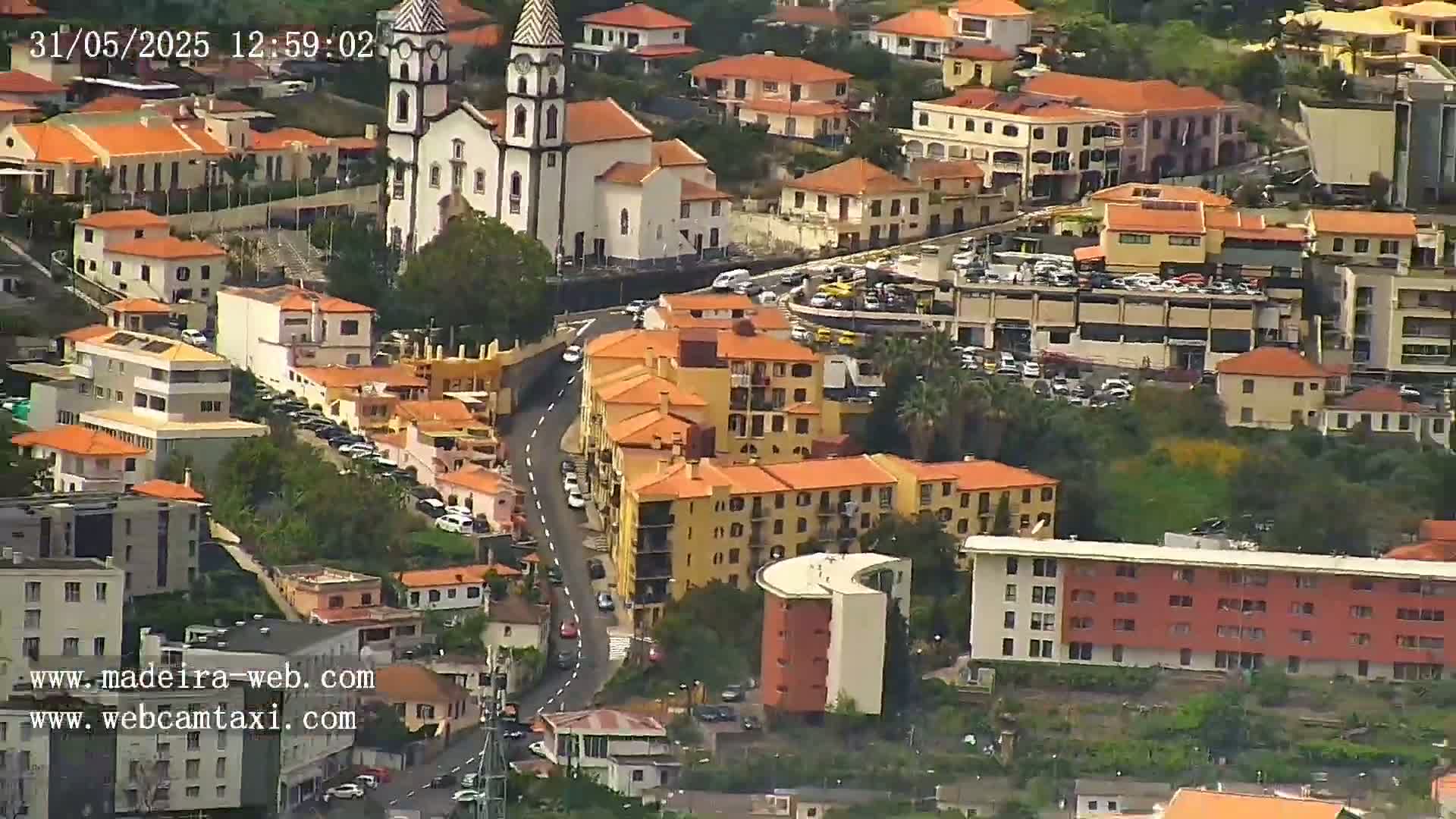 An aerial view of a town with predominantly orange-roofed buildings, a prominent white church, and a winding road, on a clear day.