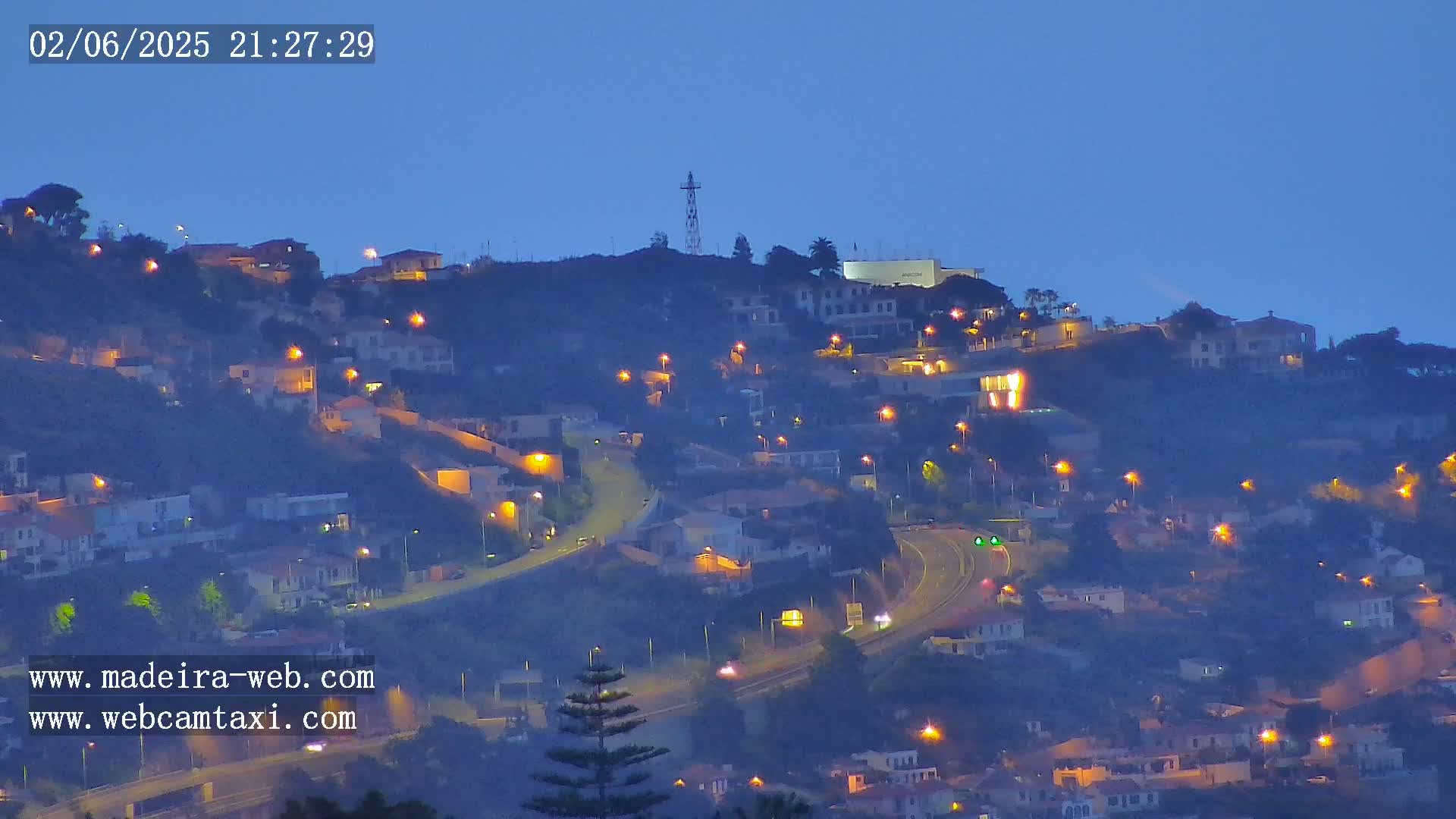 A hillside town at night is illuminated by streetlights under a twilight sky.
