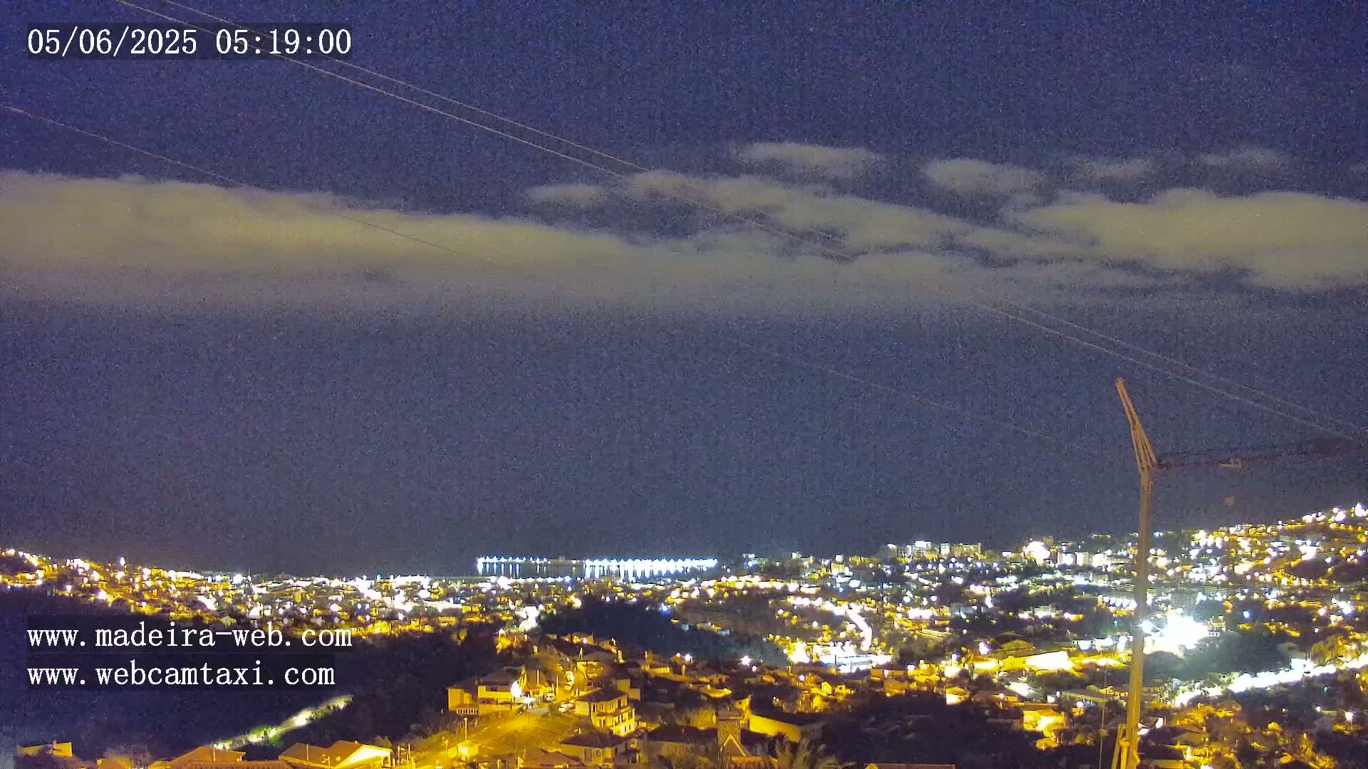 A nighttime view of a city illuminated with lights under a mostly clear sky with a thin layer of clouds.