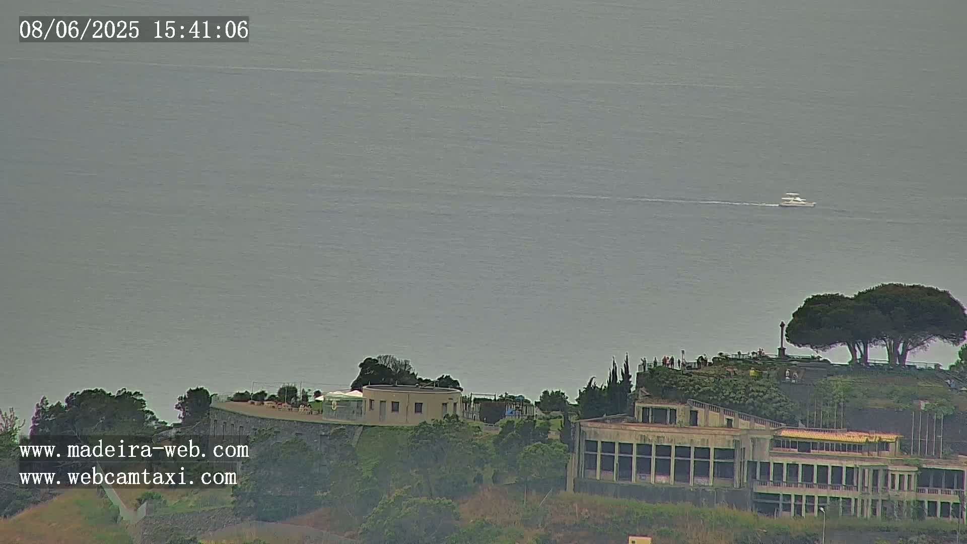 A distant boat is visible on a calm, gray ocean, with a building and several trees on a hill in the foreground.