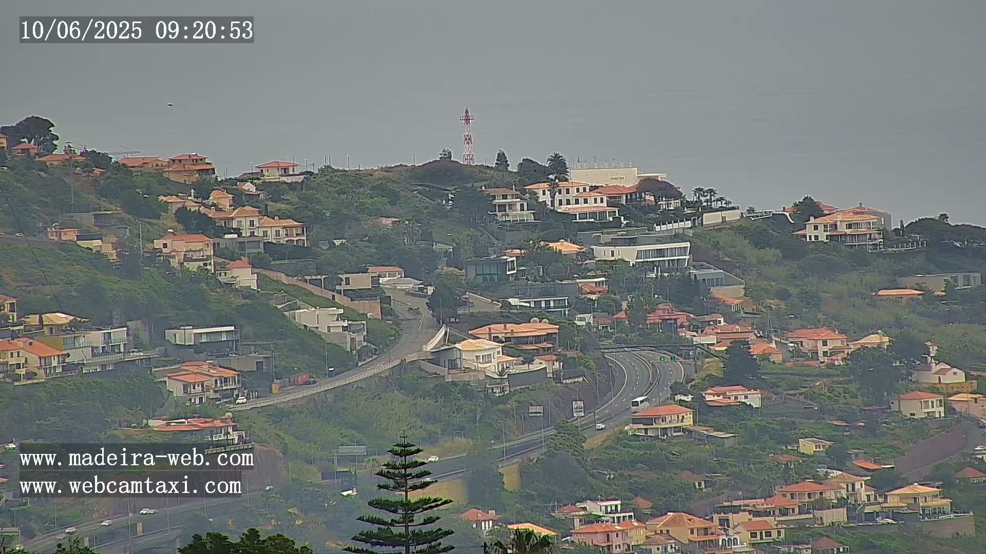 A hazy view of a hillside residential area with a highway below, overlooking a body of water.