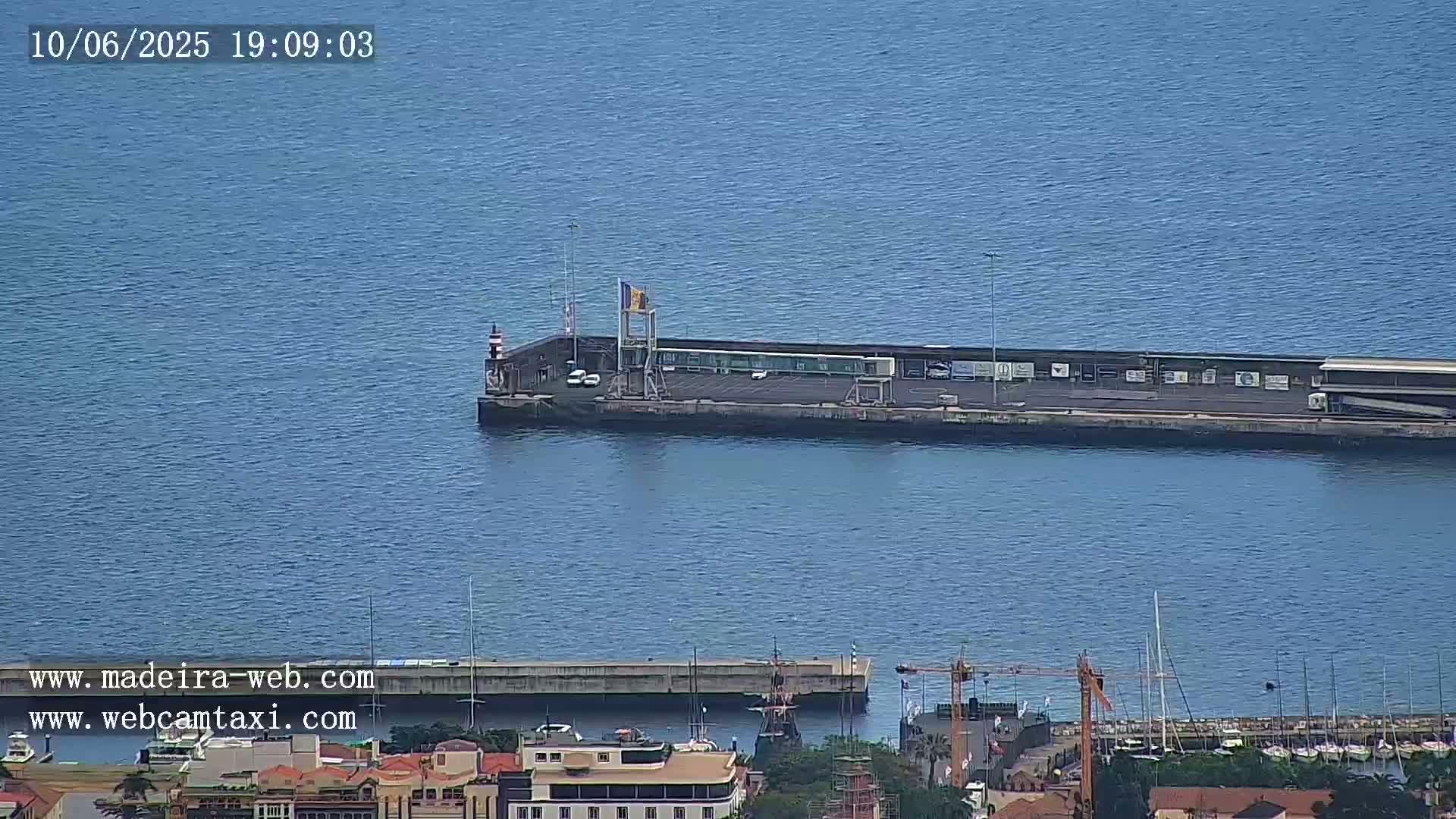 A long pier extends into a calm, blue body of water, with a harbor and town visible in the foreground.