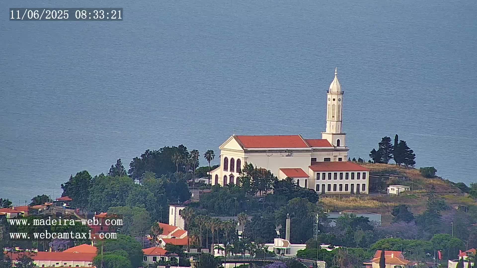 A white church with a red roof and tall steeple sits on a small hill overlooking a calm ocean.