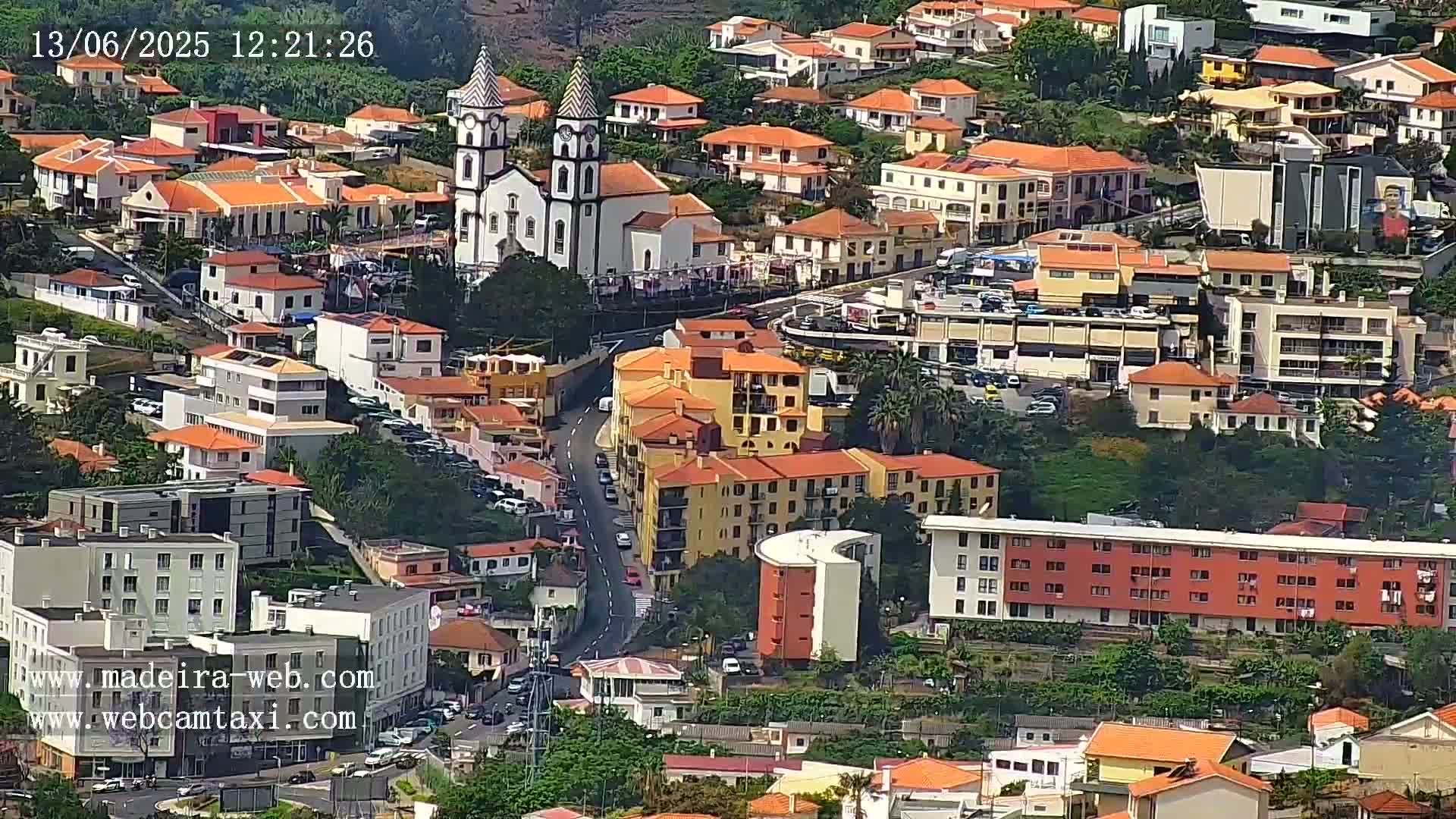 A hillside town with predominantly orange-roofed buildings, a prominent church, and a curving road, viewed on a sunny day.